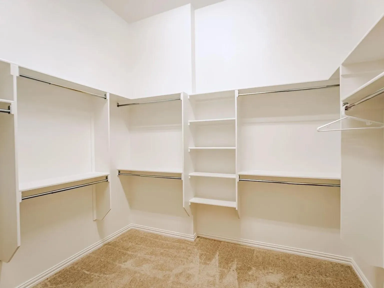 Spacious walk-in closet featuring custom white cabinetry with multiple shelving sections, dual hanging rods, and abundant storage throughout