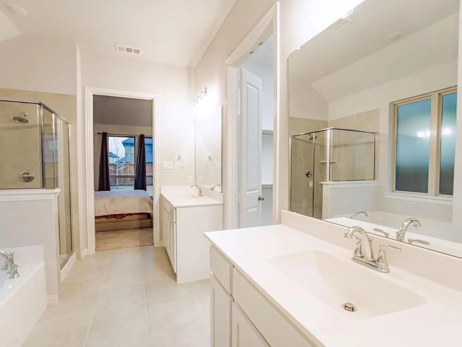 Dual vanities with white cabinetry, a glass-enclosed shower, a built-in bathtub, and neutral tile flooring