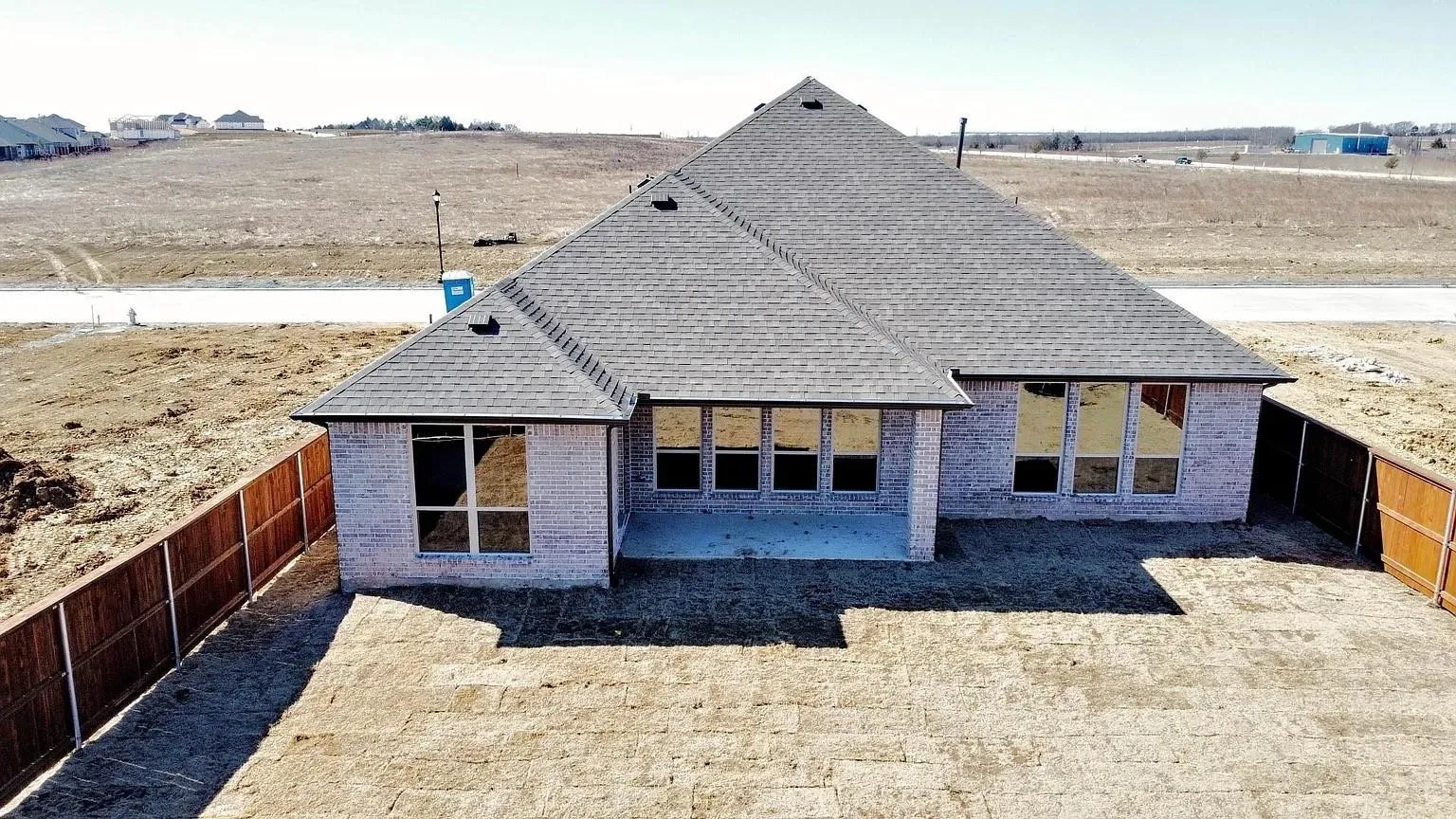 Brick exterior with a covered patio, multiple large windows, and a privacy fence