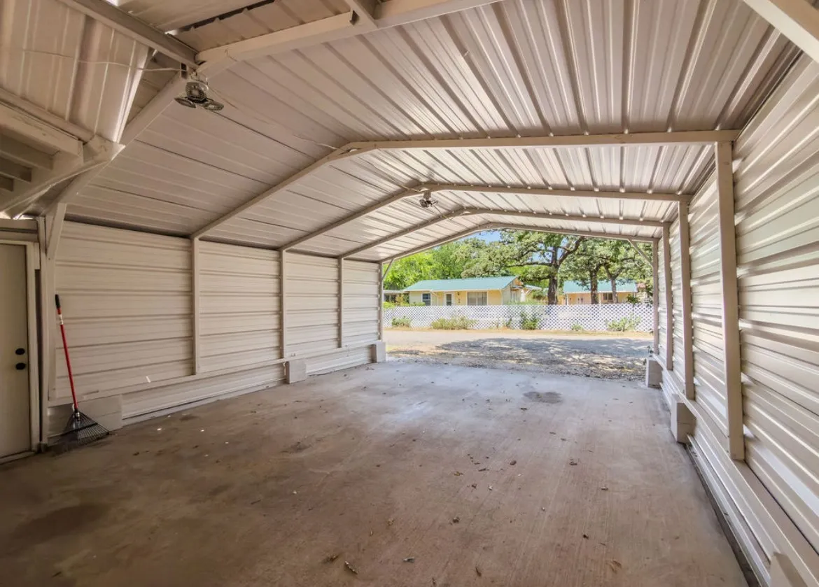 Metal carport structure with a concrete floor, corrugated metal roof, and integrated lighting fixtures