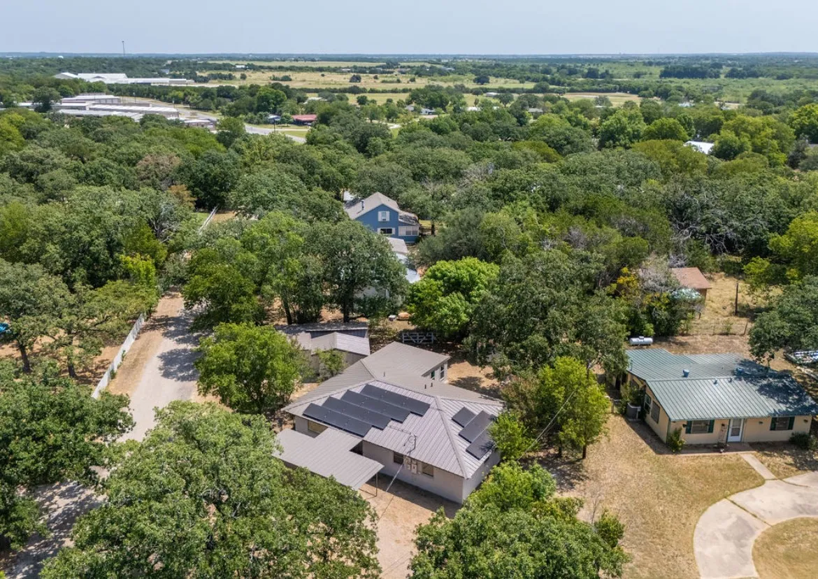 Aerial property view featuring a metal roof, solar panels, and mature trees