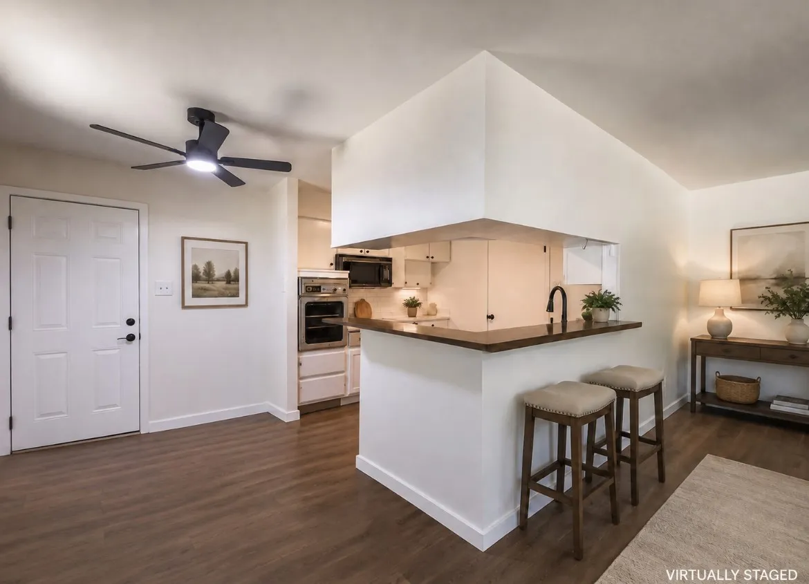Open-concept kitchen and living area featuring wood-finish flooring, a breakfast bar with a dark countertop, white cabinetry, and stainless-steel appliances including a wall oven and microwave
