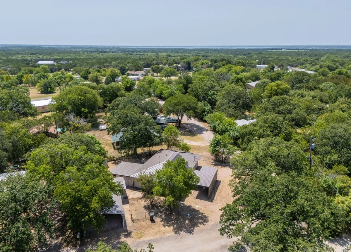 Aerial perspective showcasing a single-story residence with a light-colored roof, surrounded by mature trees