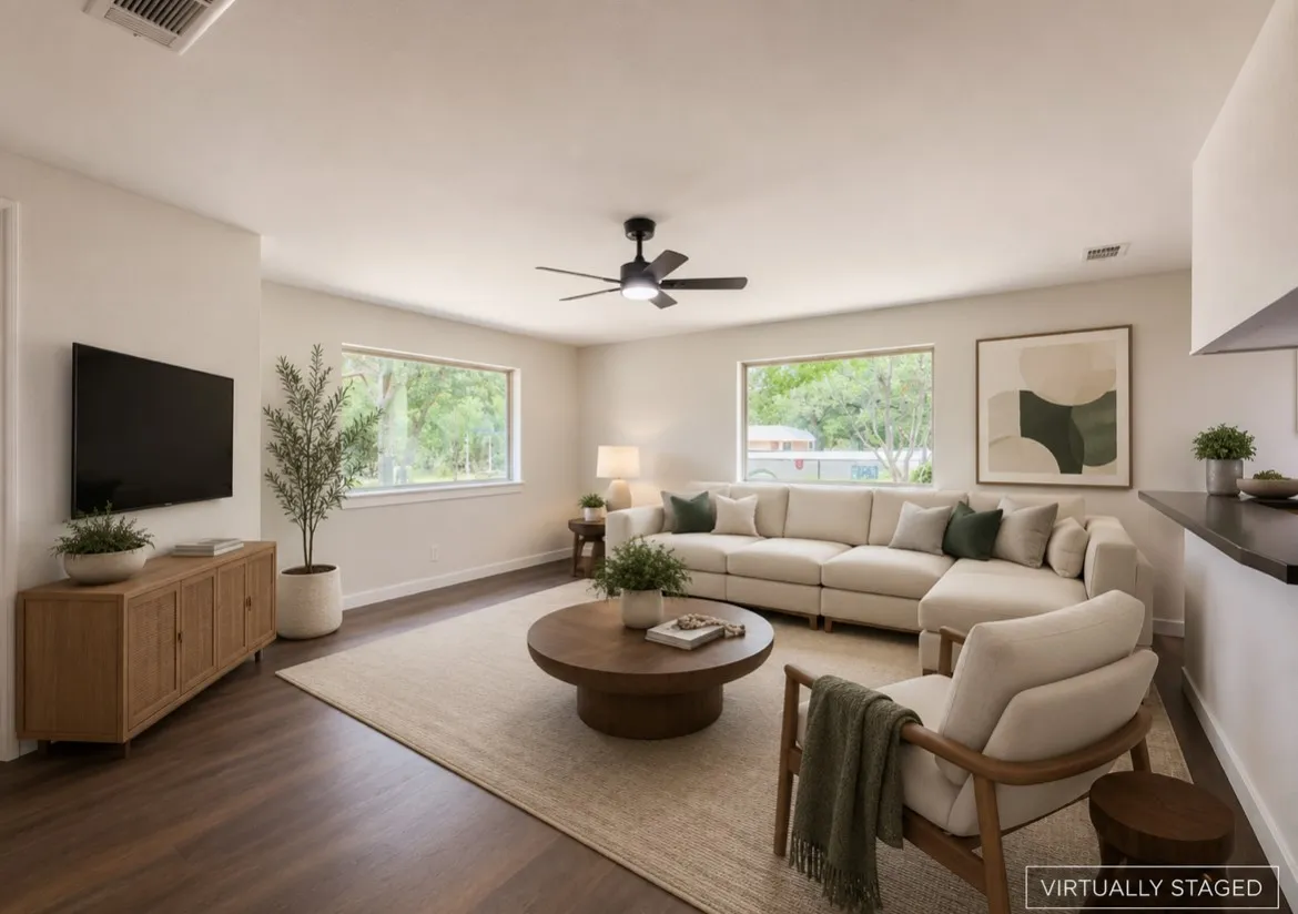 Spacious living area featuring wood-finish flooring, light neutral wall tones, and multiple large windows