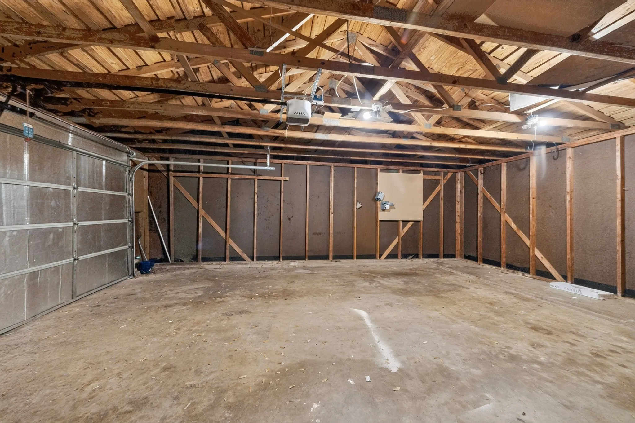 Garage space featuring a concrete floor, exposed wood ceiling beams, a paneled garage door, and a garage door opener