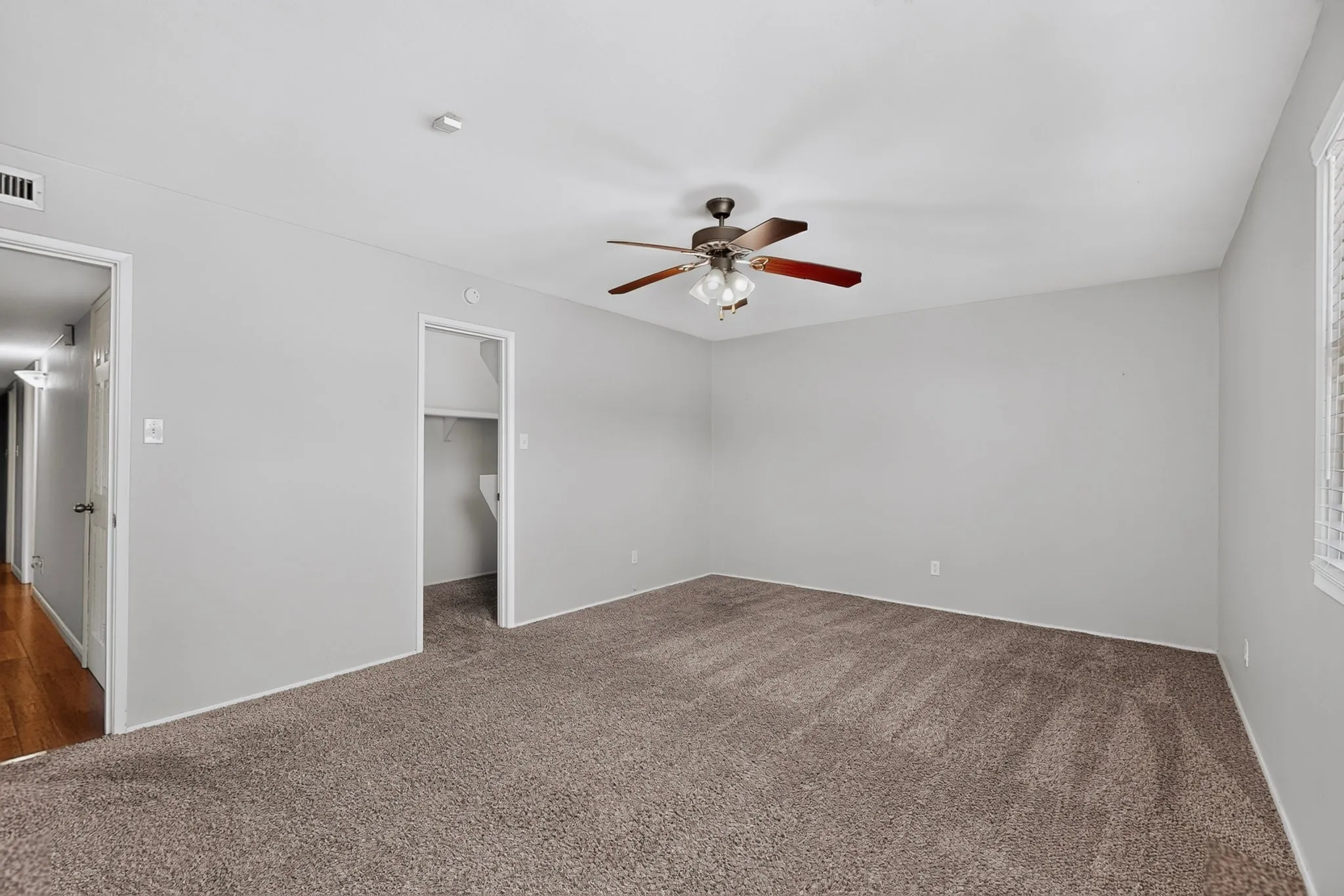 Neutral-toned carpeting, ceiling fan with light fixture, window with horizontal blinds, and a built-in closet