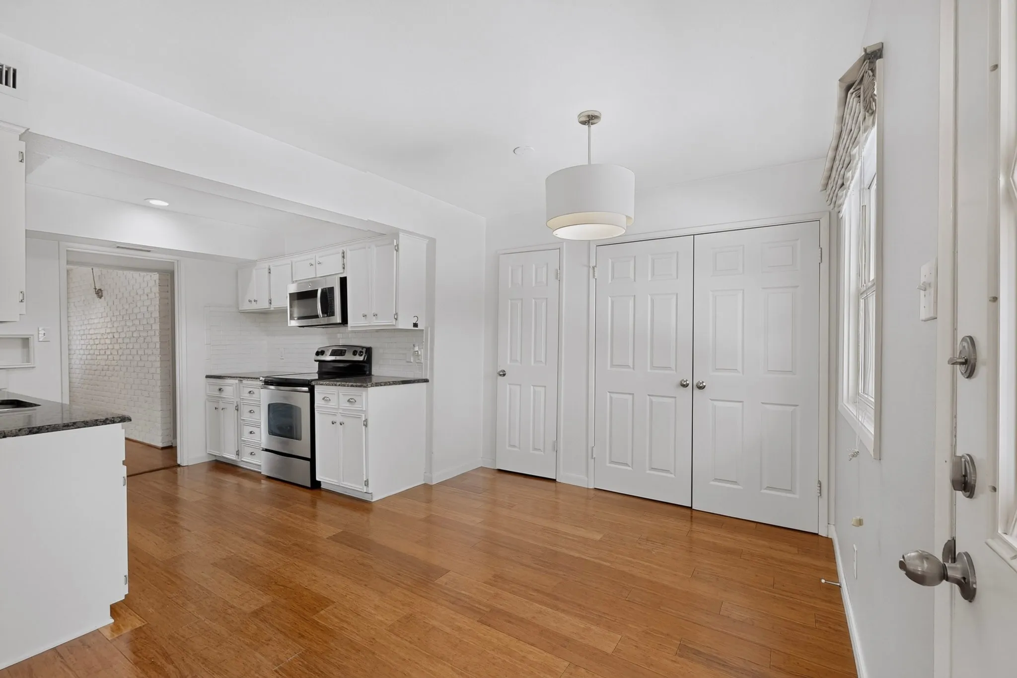 Wood-finish flooring, white cabinetry, stainless steel appliances, white subway tile backsplash, and a modern drum pendant light