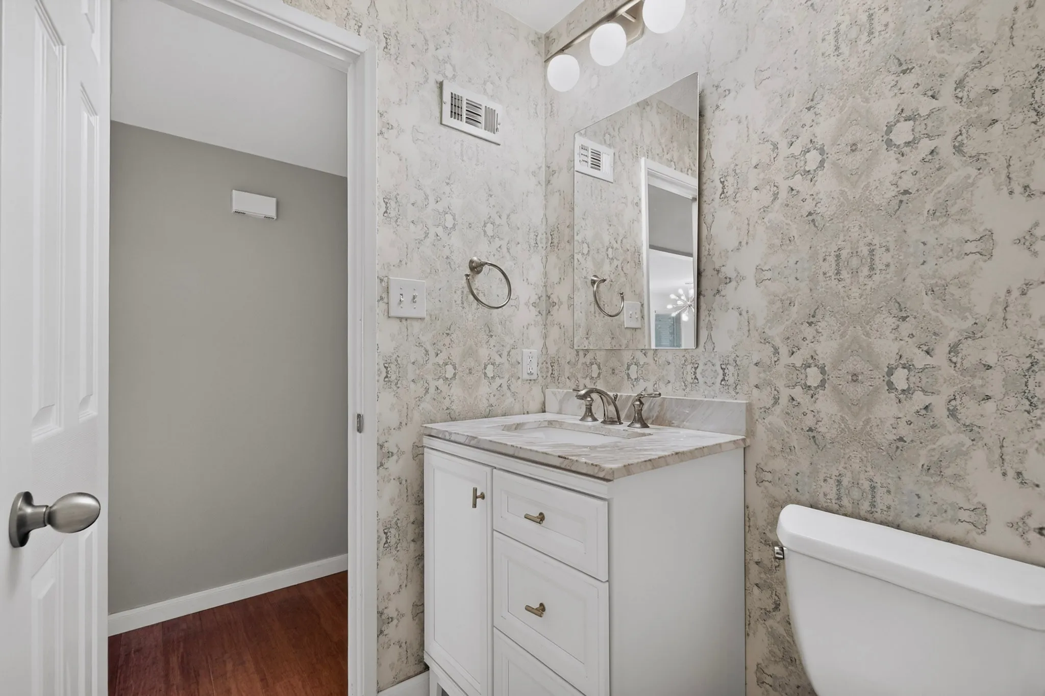 Vanity with a light-toned countertop, white cabinetry with brass-finish hardware, and a coordinating wall-mounted light fixture