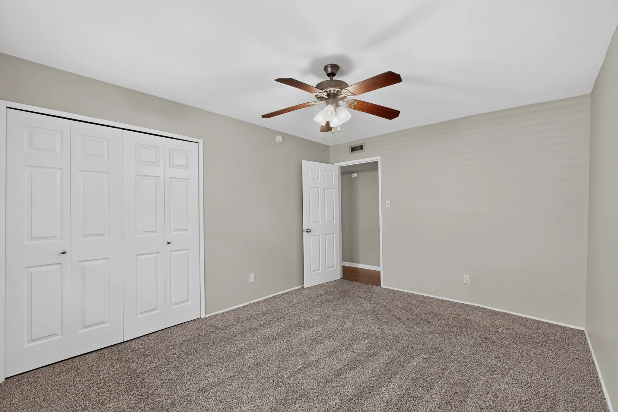Neutral gray wall paint, textured carpeting, bi-fold closet doors, paddle ceiling fan with integrated lighting