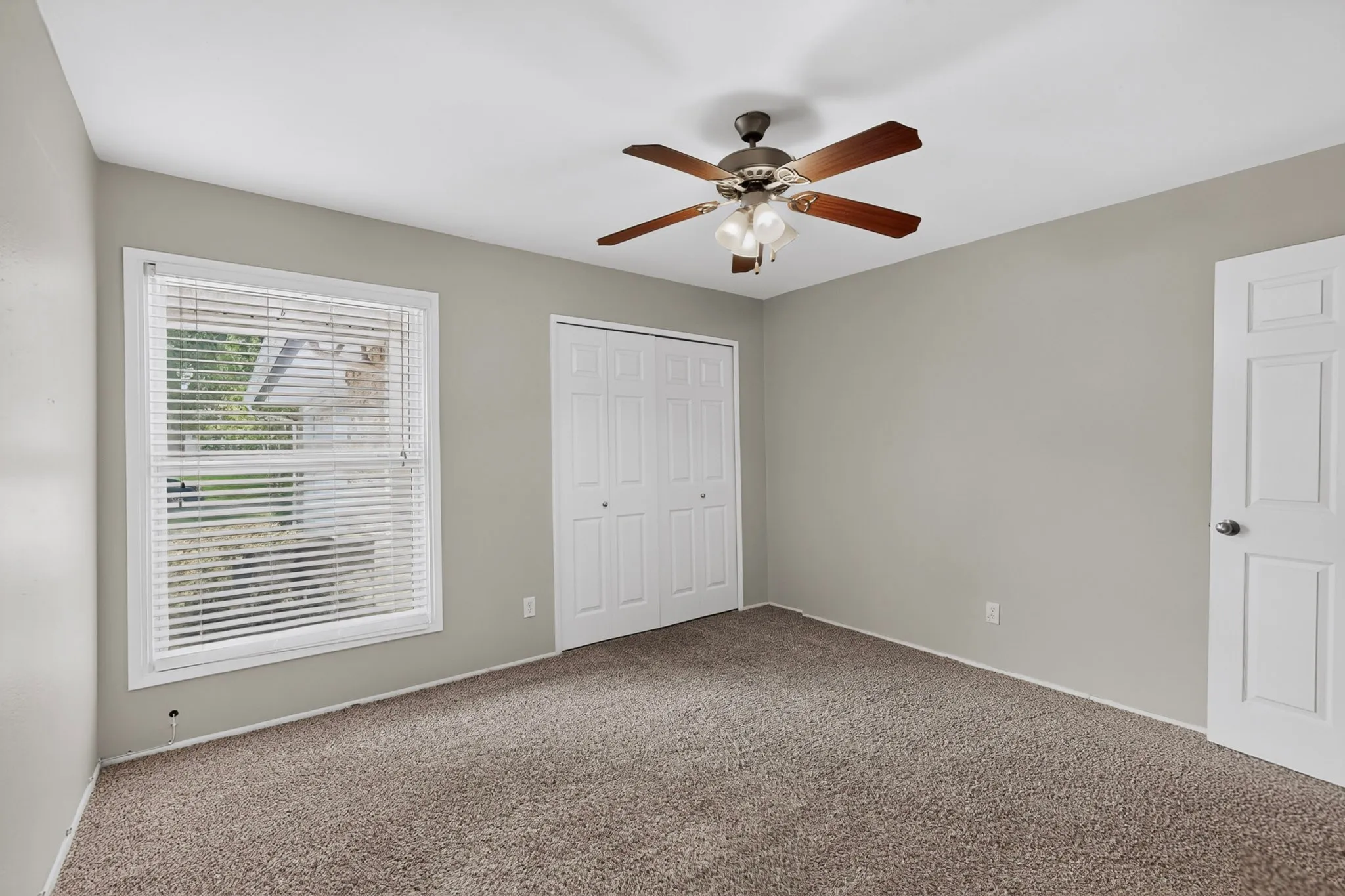 Wall-to-wall carpeting, window with blinds, ceiling fan with integrated lighting, bi-fold closet doors, and painted interior door
