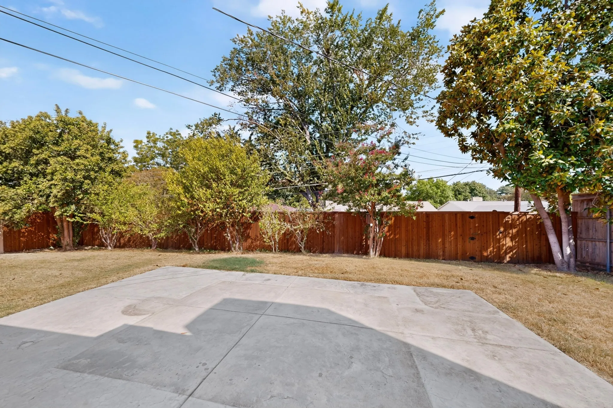 Expansive backyard featuring a concrete patio, a manicured lawn, a privacy fence, and mature trees