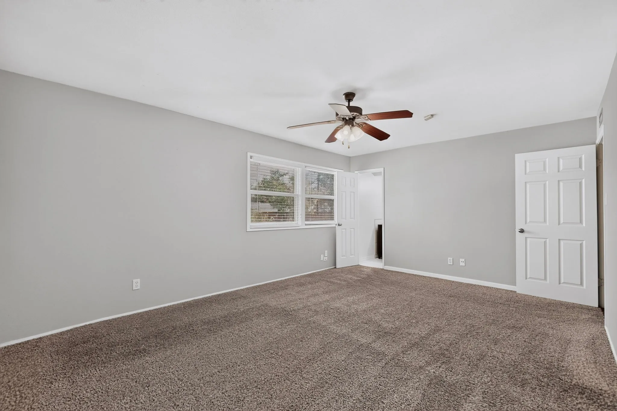 Spacious room featuring neutral carpet flooring, light gray wall paint, and a ceiling fan with integrated lighting