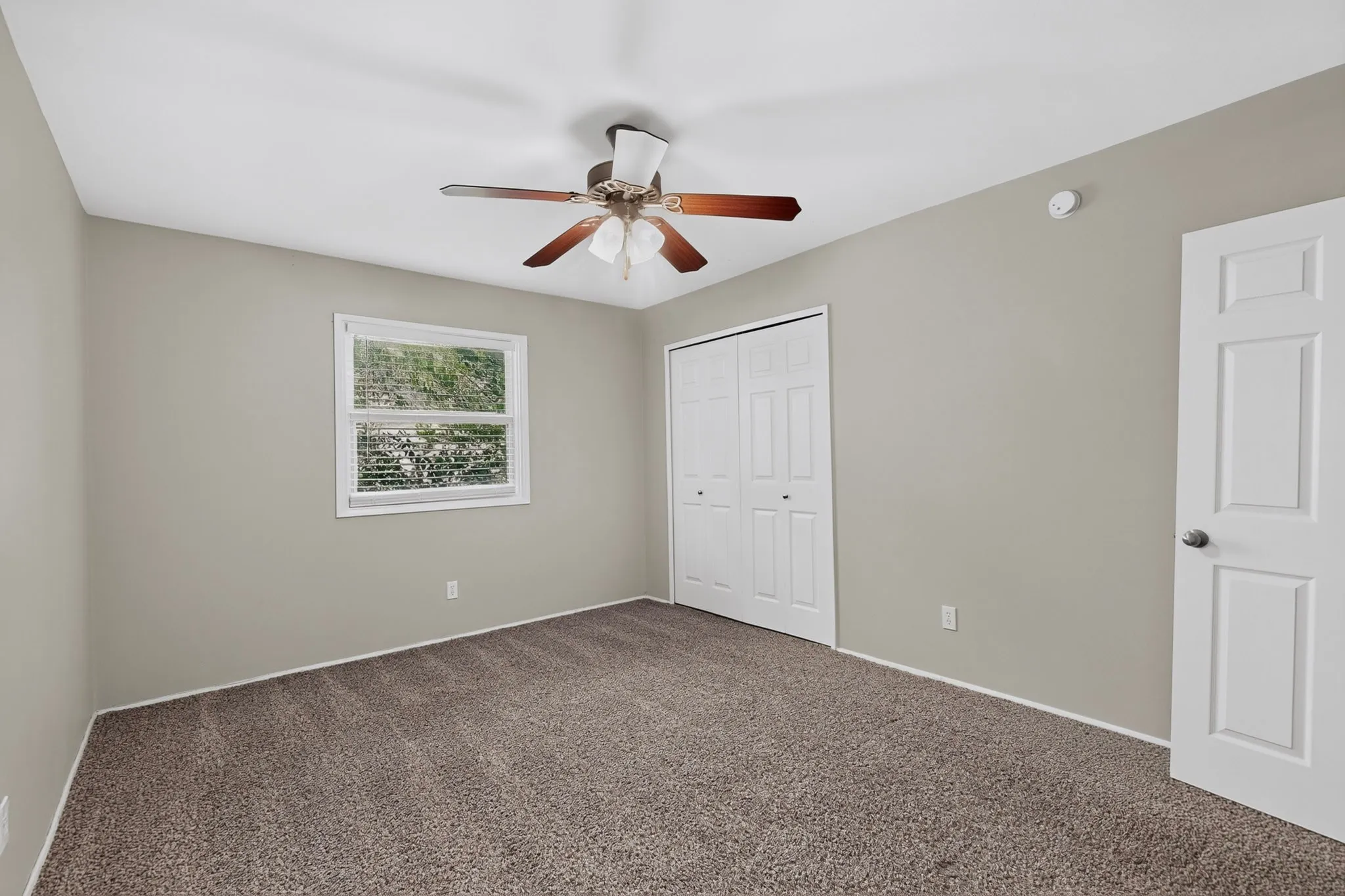Neutral-toned walls, plush carpet flooring, and a ceiling fan with light fixture