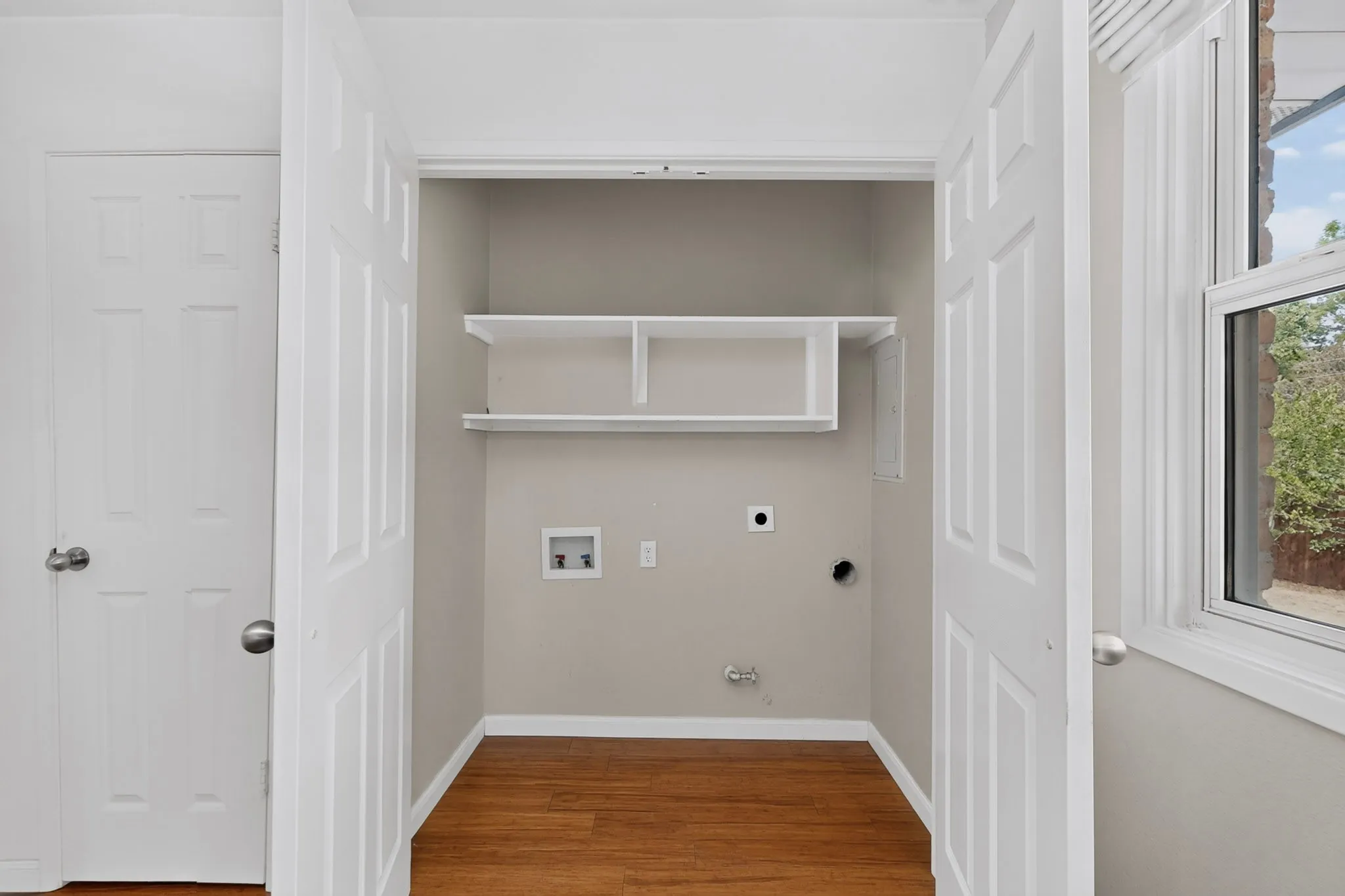 Laundry area featuring wood-finish flooring and integrated shelving