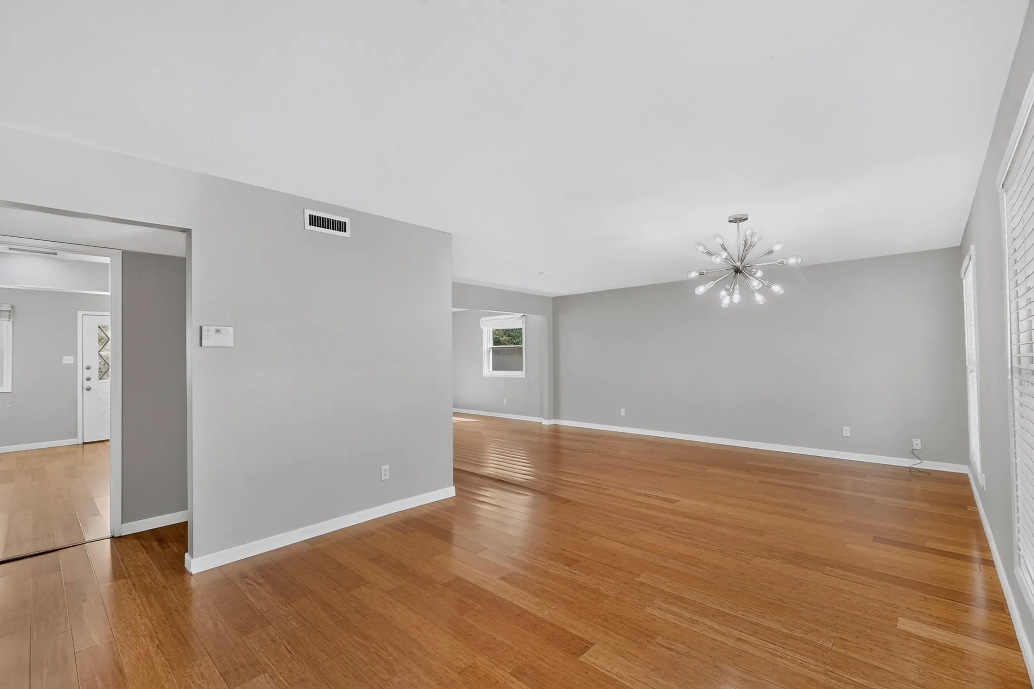 Hardwood flooring throughout, modern sputnik chandelier, large windows with horizontal blinds, neutral wall paint, and white trim