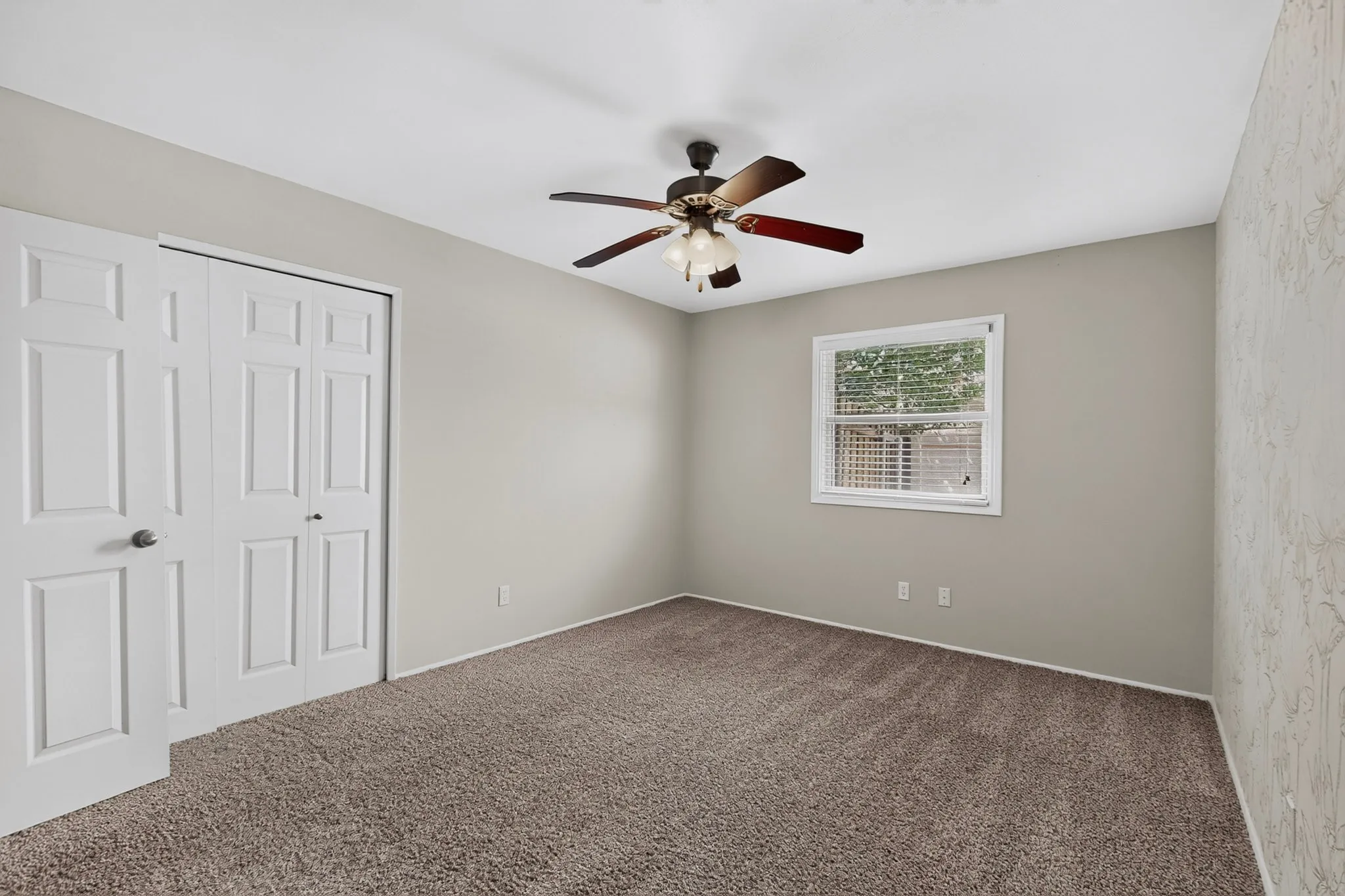 Carpeted room featuring a ceiling fan with integrated lighting, a window with blinds, and white bi-fold closet doors