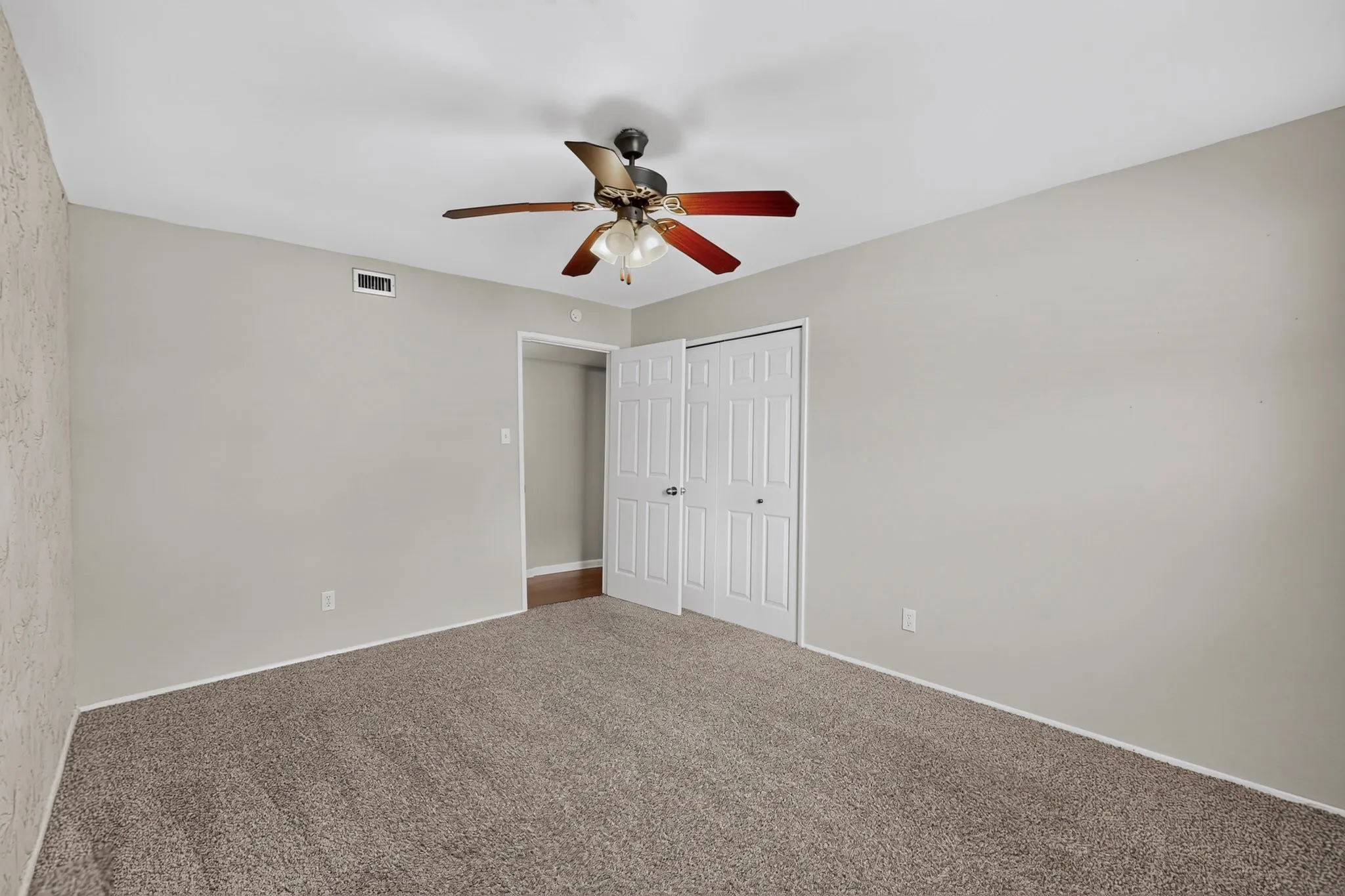 Neutral-toned walls, textured accent wall, brown carpet flooring, bi-fold closet doors, and a ceiling fan with light fixture