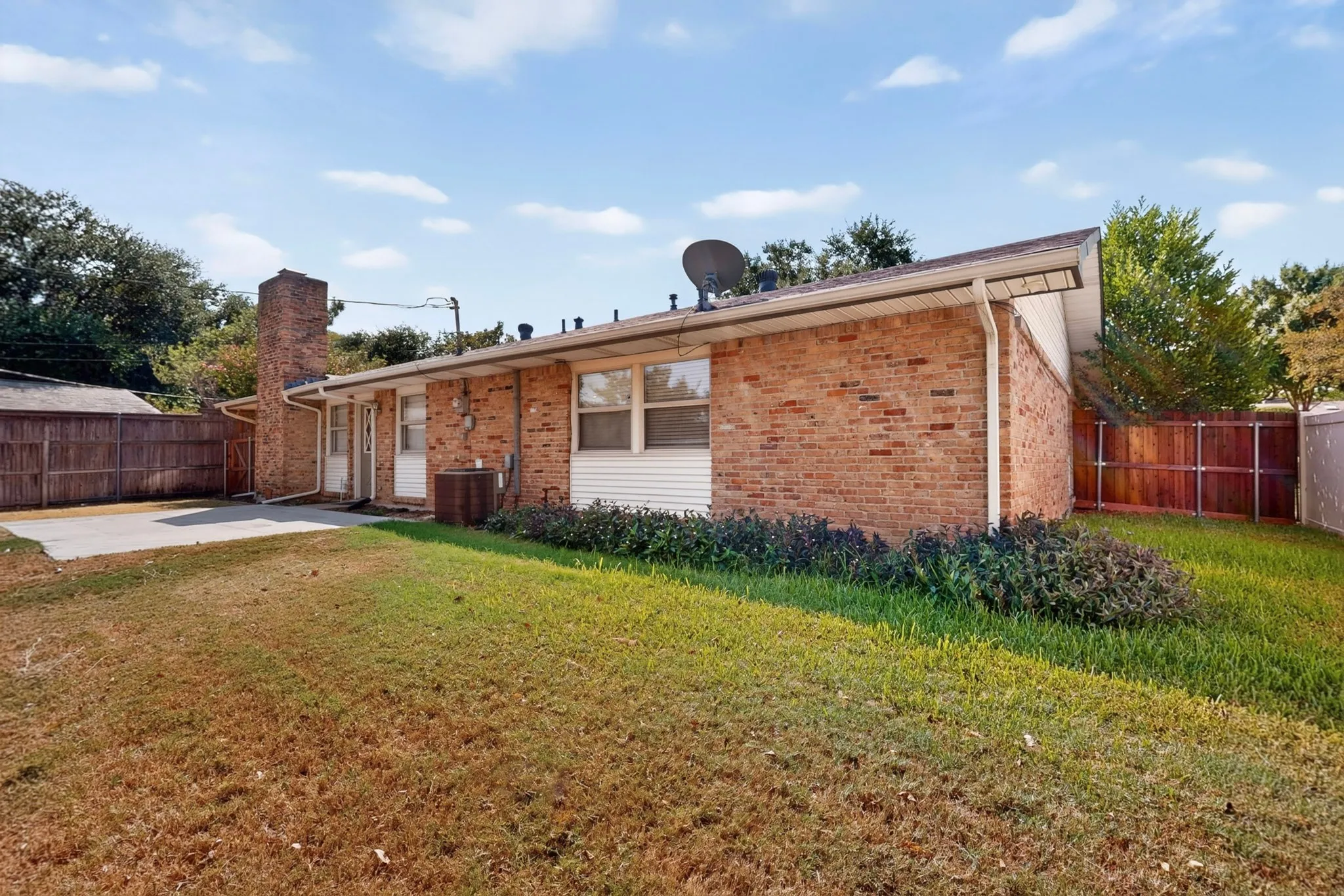 Brick exterior with a prominent chimney, concrete patio, and a wood privacy fence