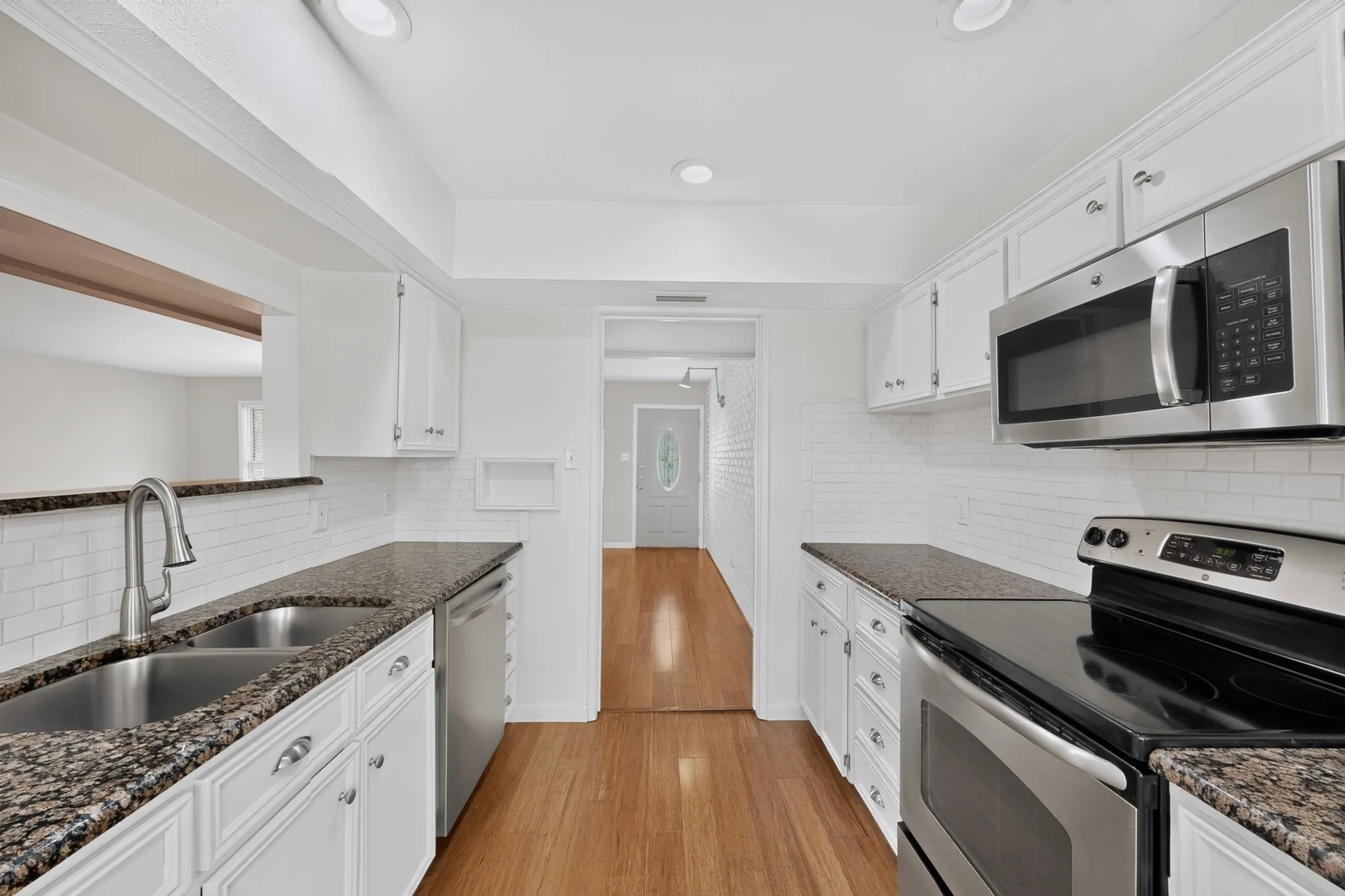 White cabinetry, granite-finish countertops, stainless steel appliances, subway tile backsplash, and wood-finish flooring