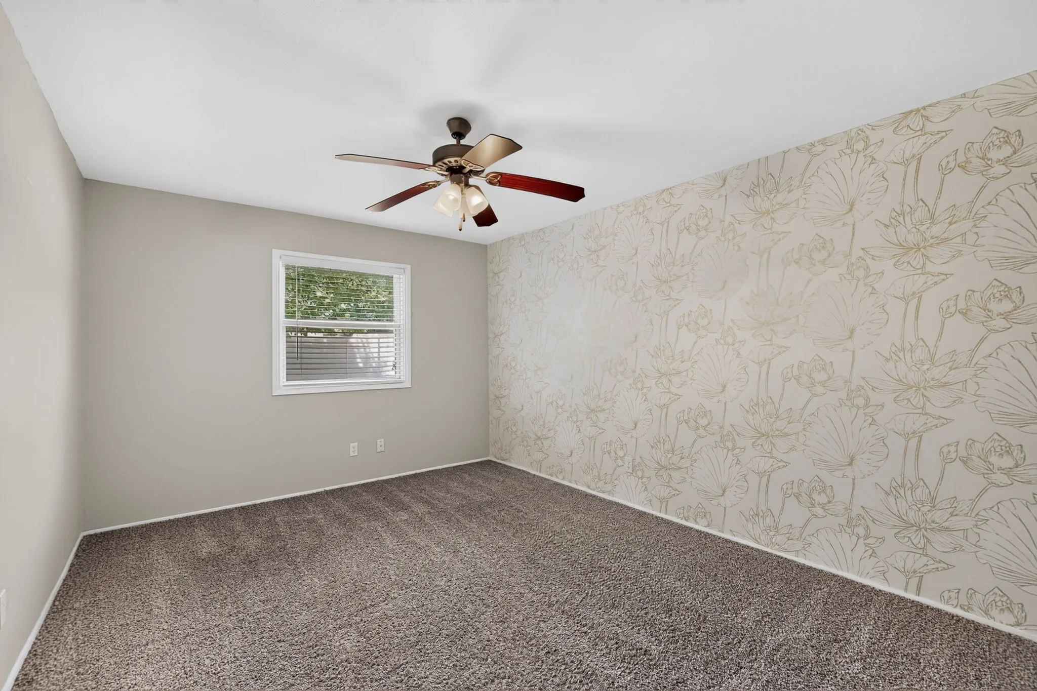 Neutral wall paint, ceiling fan with integrated lighting, window with blinds, patterned accent wall, and carpet flooring