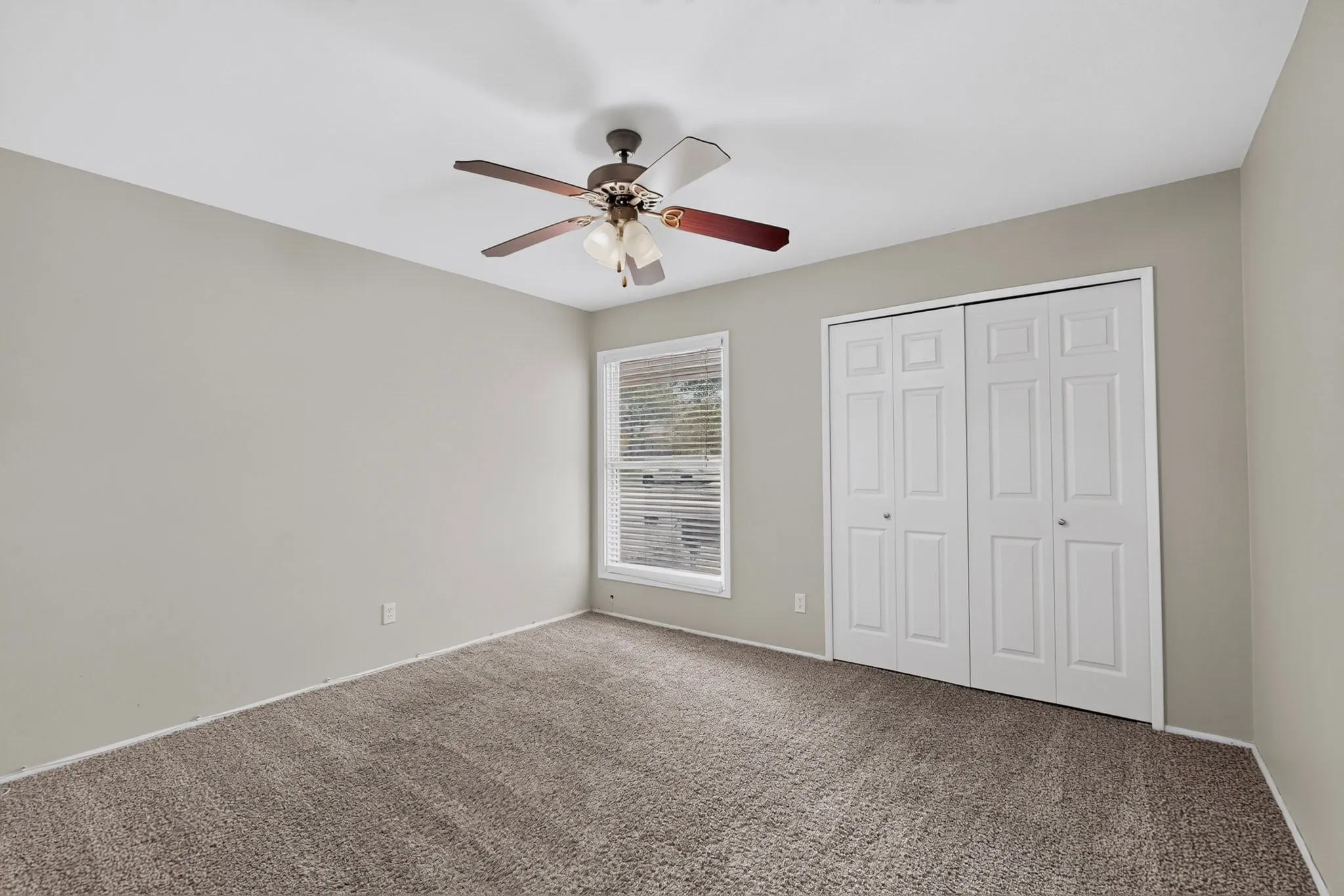 Neutral wall color, carpet flooring, window with blinds, bi-fold closet doors, and a ceiling fan with integrated lighting