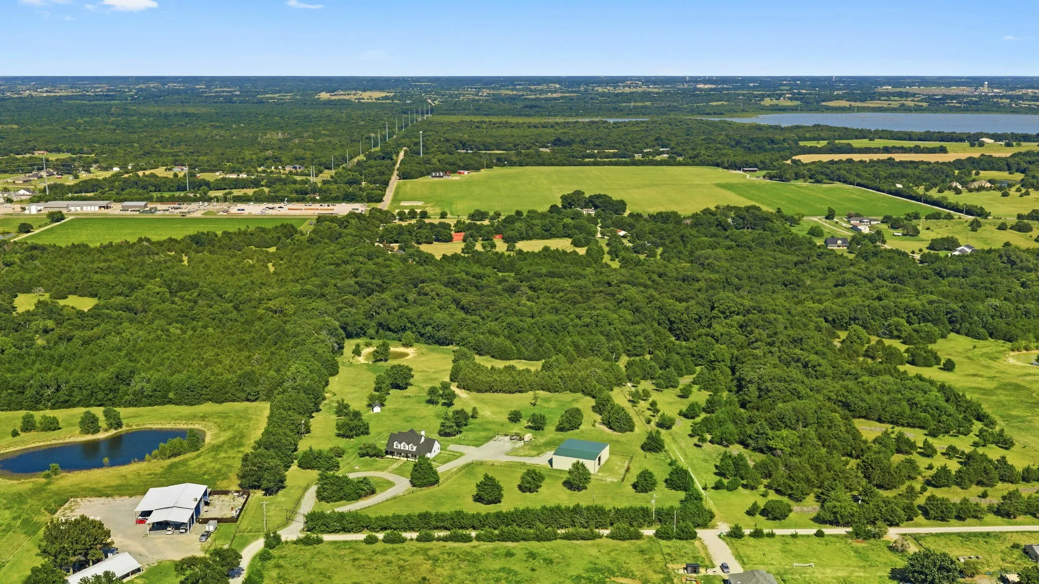 Looking east, a sweeping canopy of mature trees and peaceful neighboring acreages surrounds the property, with Lake Lavon visible in the upper right of the aerial view completing the beautiful country setting.