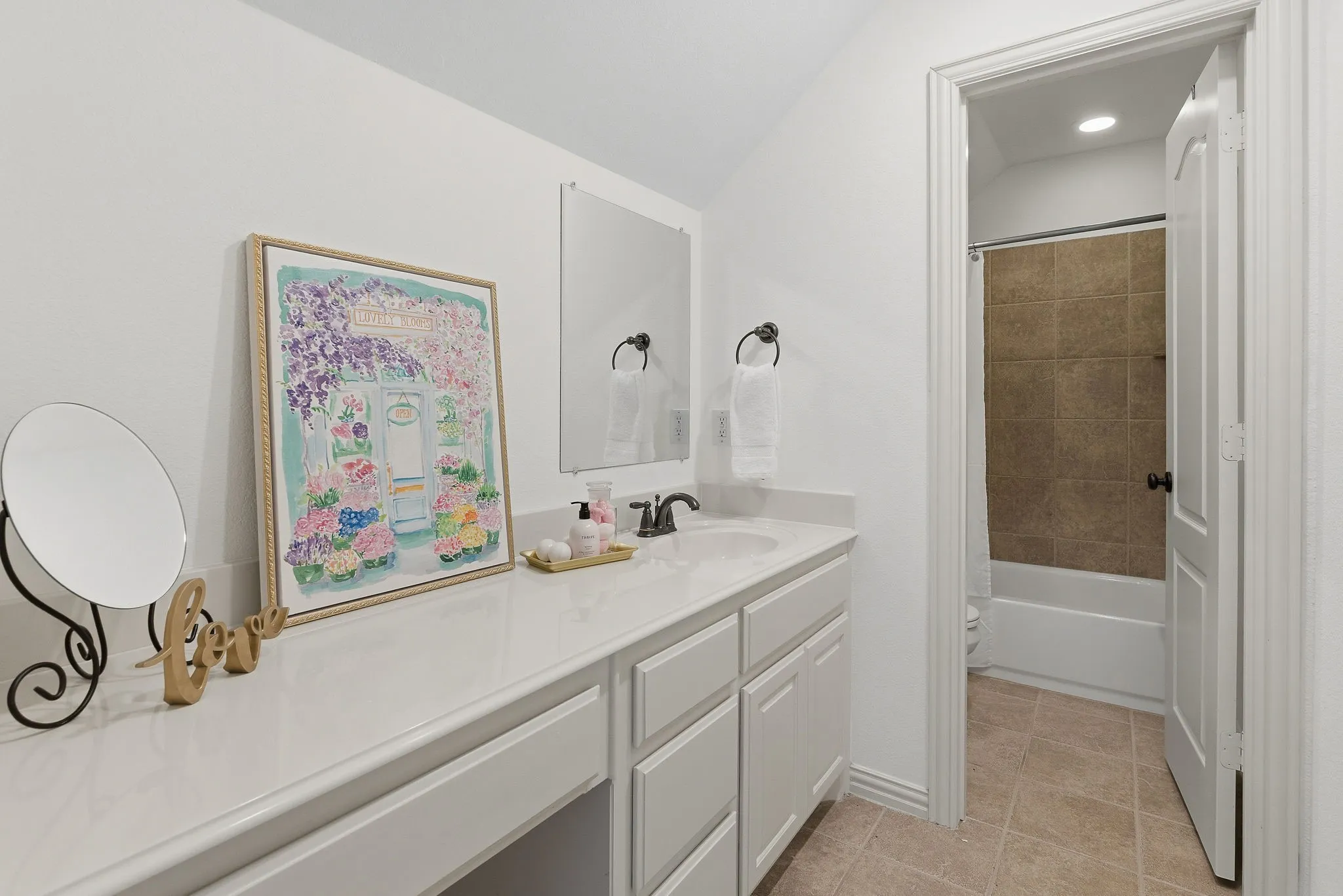 The upstairs bedroom’s private en suite bath offers an extended white vanity with generous counter space, built-in drawers and cabinetry, and a separate bathing area with a tile-surround tub and shower for added privacy and convenience.
