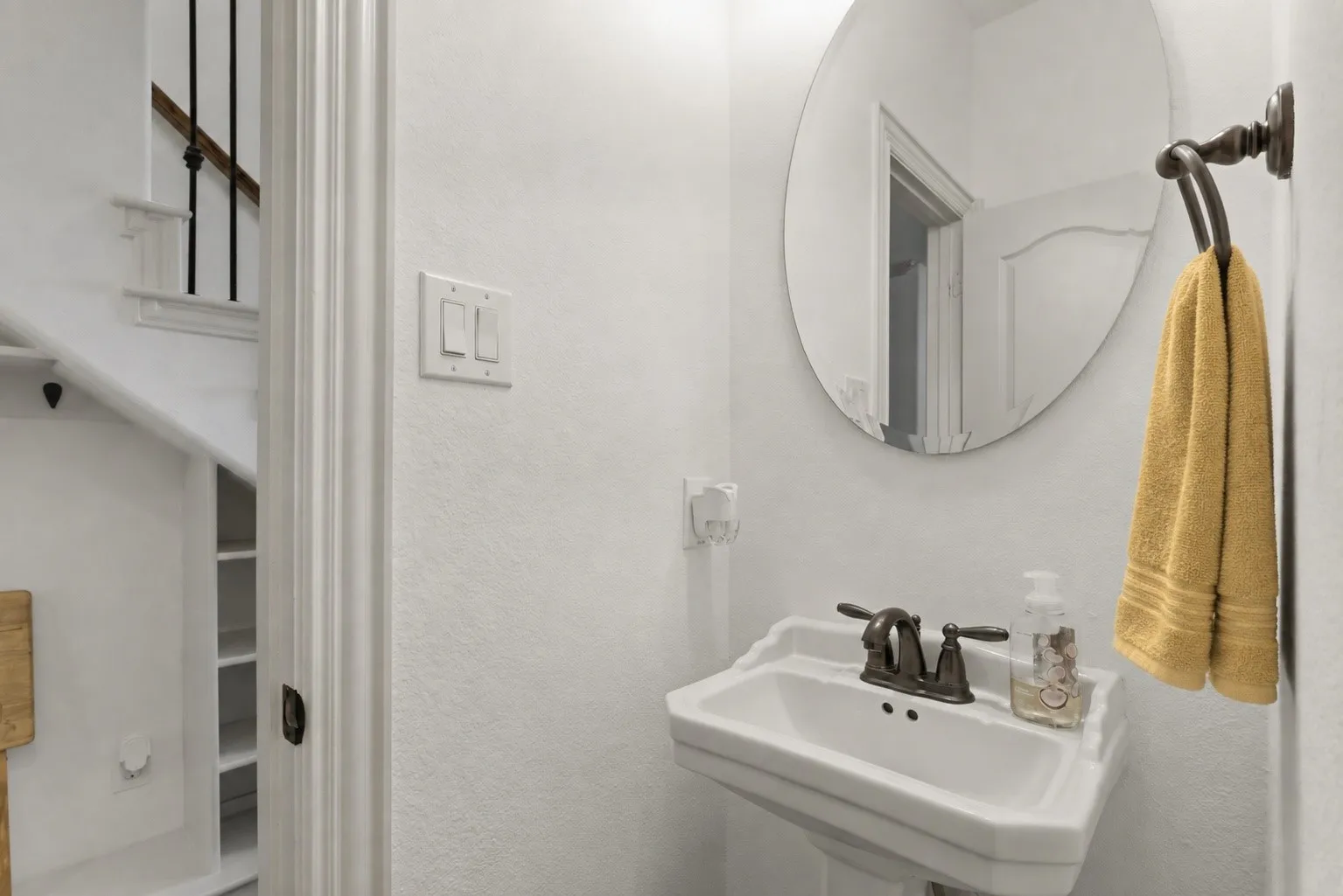 Conveniently located off the kitchen, this guest half bath features a classic pedestal sink, with a nearby drop zone offering built-in cubbies and hooks to keep everyday essentials organized as you enter from the back door.