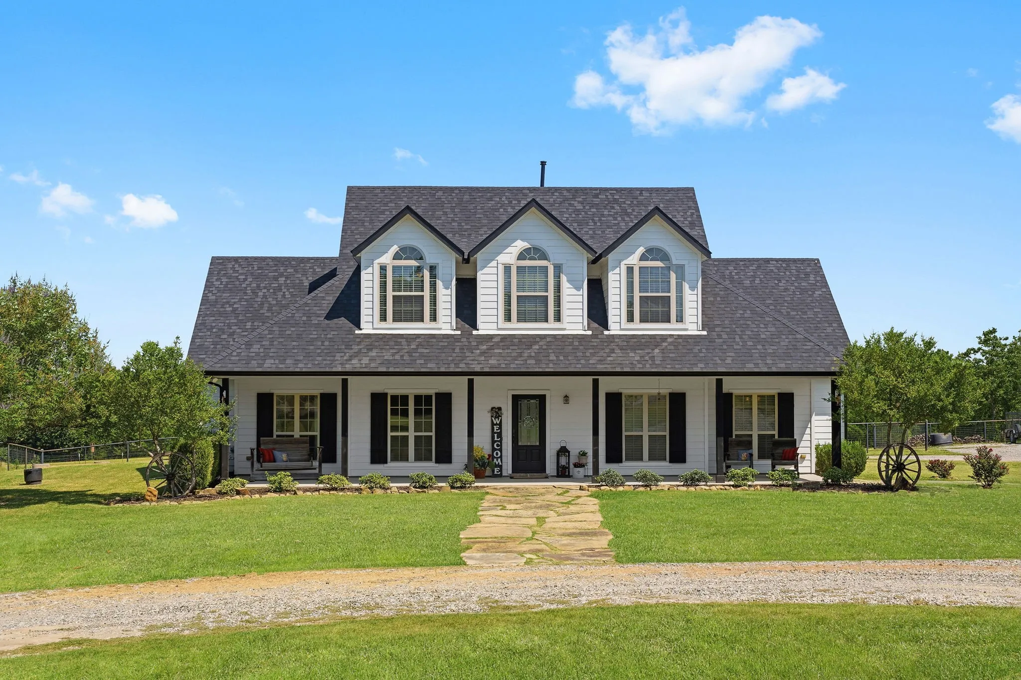 Classic white siding, contrasting dark shutters, and three graceful dormers frame an expansive covered porch, with a stone walkway leading through the lawn to your front door.