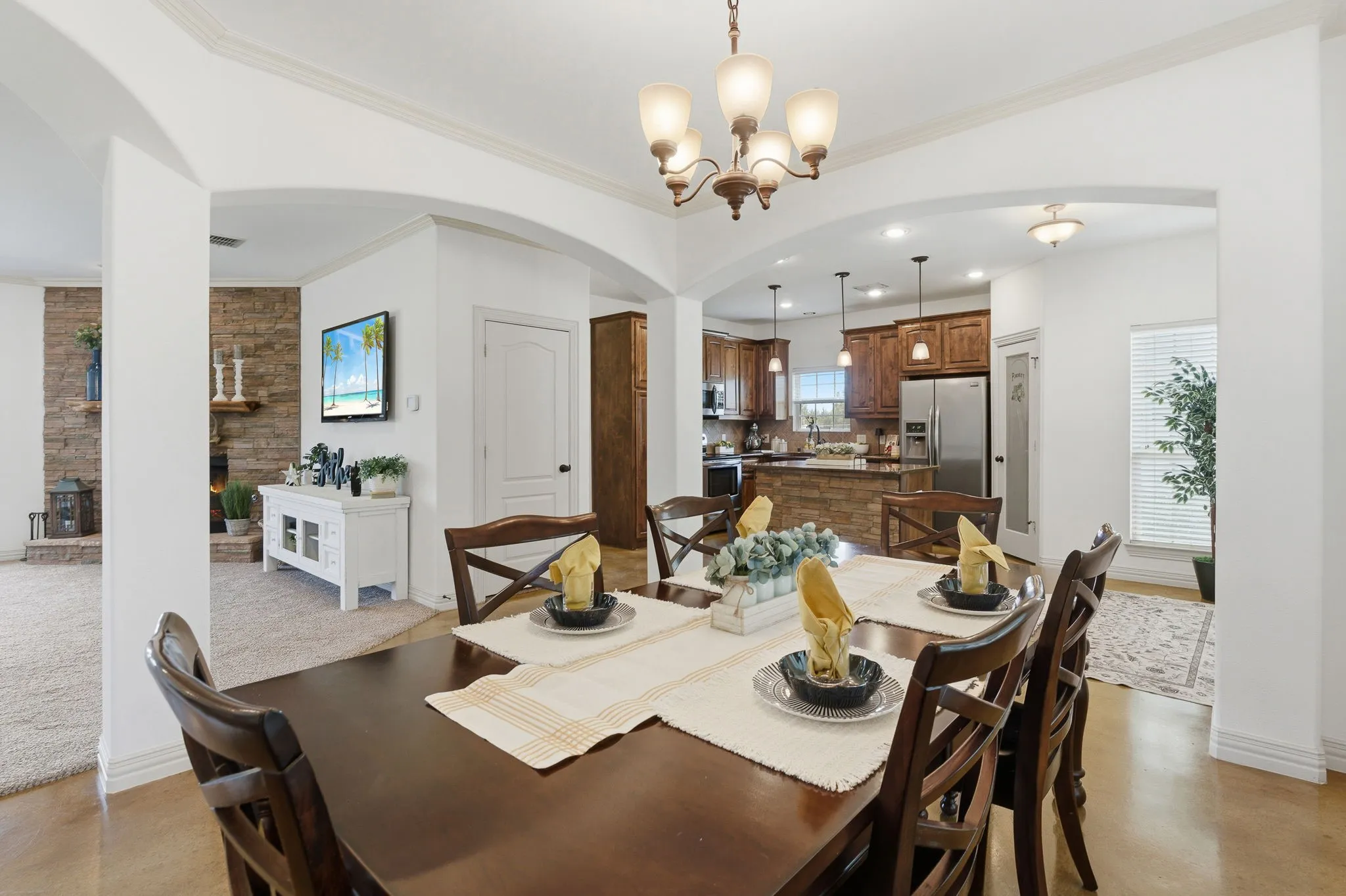 Graceful archways connect the formal dining room to the kitchen’s rich wood cabinetry and stone-accented island, while the family room’s stone fireplace to the left creates a warm backdrop for gathering and entertaining.