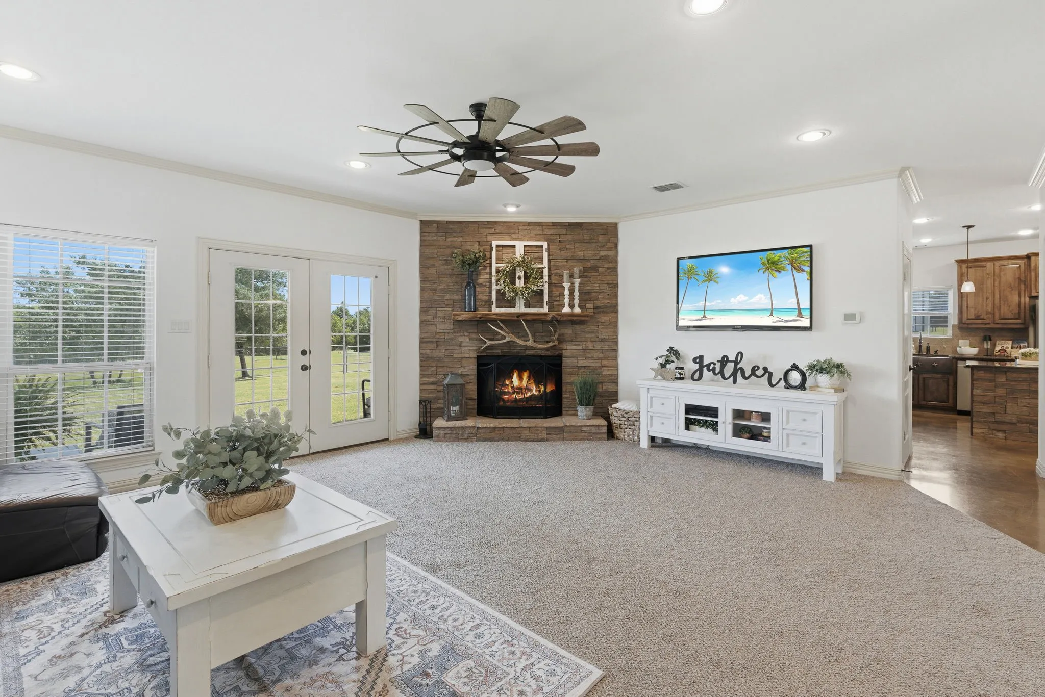 A striking stone wood-burning fireplace with propane start anchors this inviting family room, where soft carpeting, crown molding, and glass patio doors overlooking the grounds create a welcoming setting for relaxed evenings and memorable gatherings.