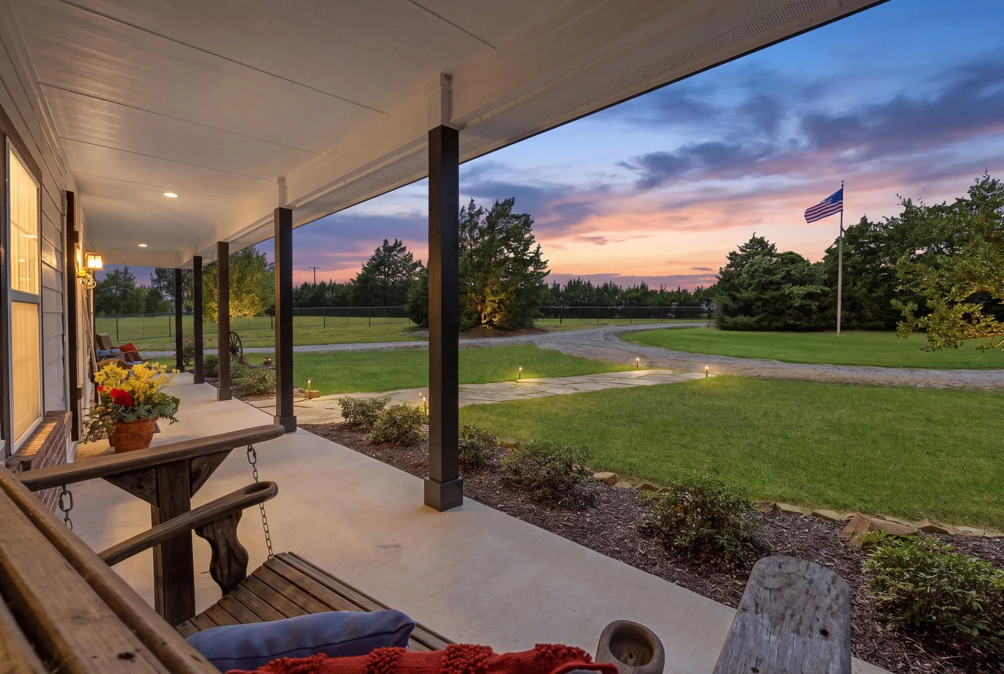 Unwind on the covered front porch as twilight settles over the spacious lawn, mature trees, and curving drive, offering a beautiful setting for quiet evenings and lingering conversations.