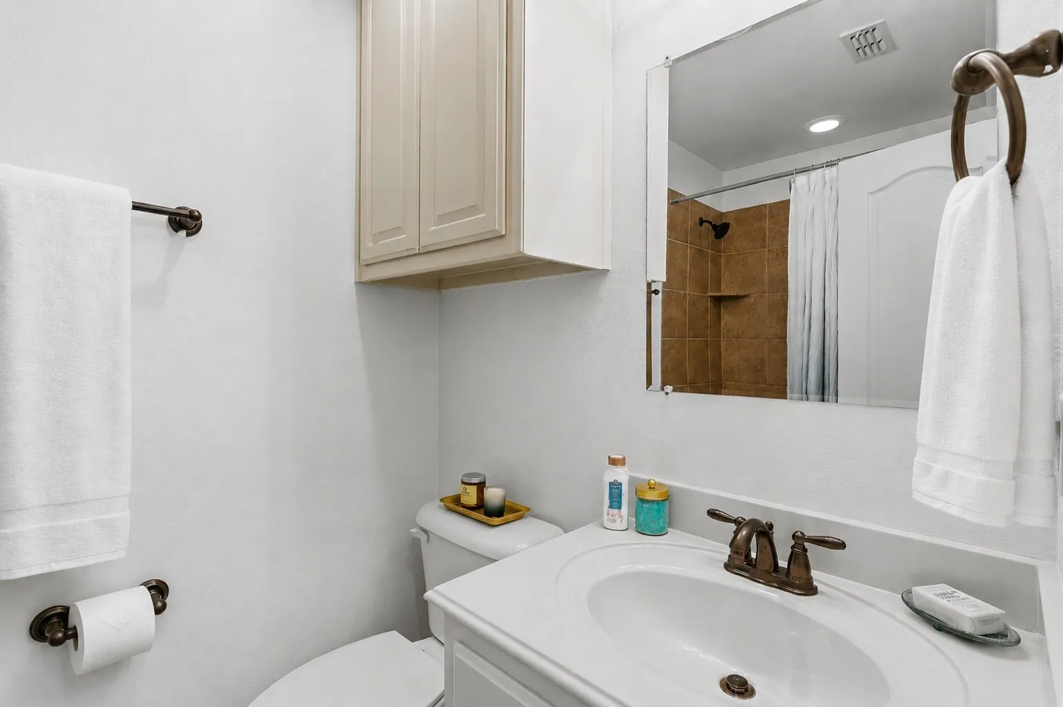 Conveniently shared by two upstairs bedrooms, this Jack and Jill bath pairs a crisp white vanity and warm bronze-tone fixtures with a tiled shower surround and overhead storage for everyday essentials.