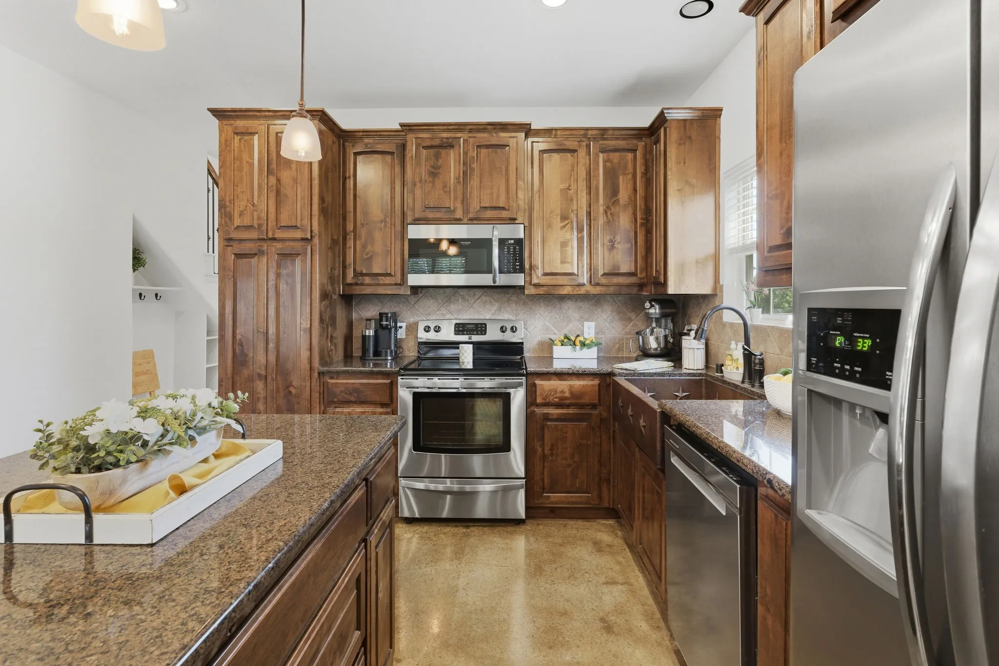 Richly stained wood cabinetry, stainless steel appliances, and generous counter space surround a central island, creating a welcoming kitchen with ample storage and room to prepare your favorite meals.