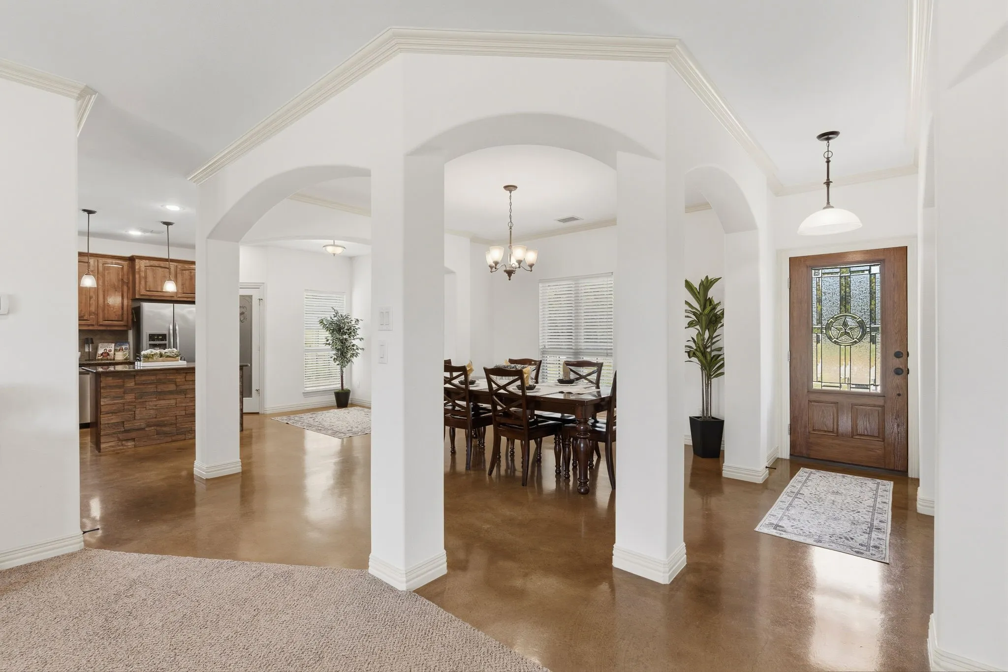 Graceful archways and crown molding frame the view from the family room into the formal dining room and welcoming entry, where warm stained concrete floors and a decorative glass front door bring character to the open layout.