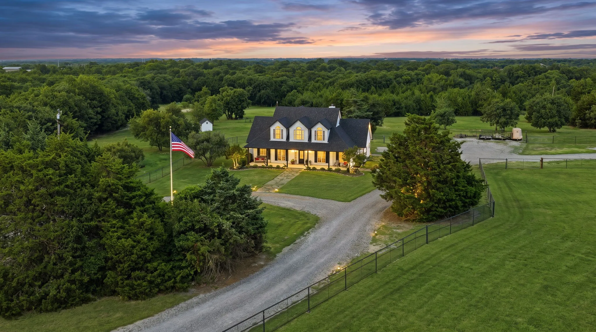 A winding drive leads through mature trees and open grounds to this warmly illuminated farmhouse, nestled on 10.4 scenic acres beneath a sweeping twilight sky for a picturesque welcome home.