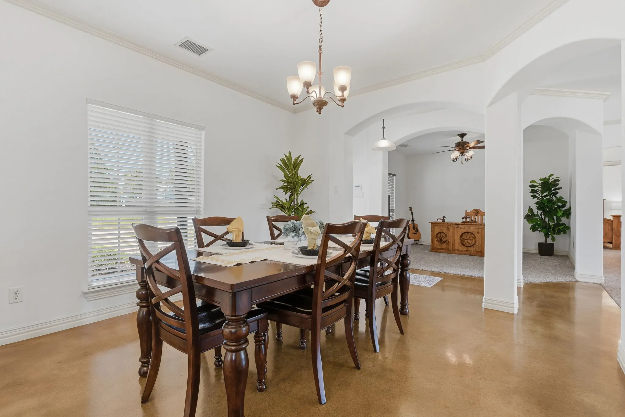 Viewed from the kitchen, the light-filled formal dining room showcases stained concrete flooring, crown molding, and graceful archways framing the entry and office, creating an inviting setting for everyday meals and special gatherings.