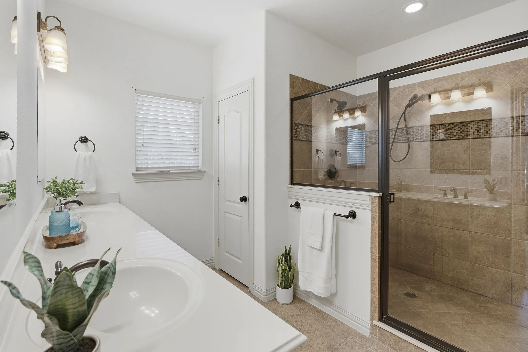 The primary bath offers a spacious glass-enclosed shower with warm tile, a mosaic accent band, and both a fixed showerhead and handheld sprayer for a relaxing daily retreat.
