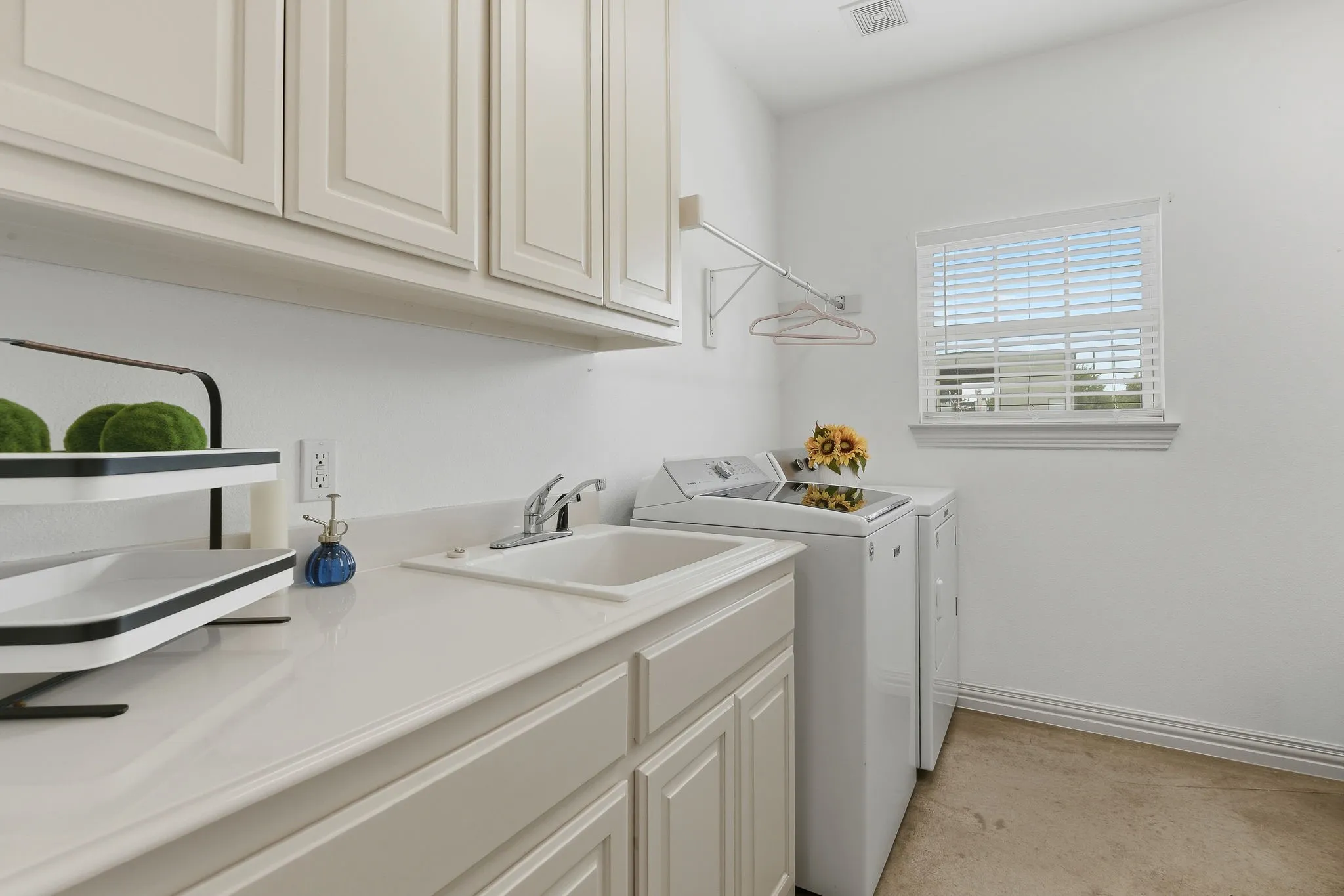 Bright and spacious, the utility room features abundant cabinetry, a generous folding counter, a utility sink, and a hanging rod, plus room for an extra refrigerator or freezer with additional storage space to spare.