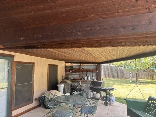 Covered patio featuring a wood-plank ceiling, concrete flooring, and an outdoor utility area with corrugated metal siding