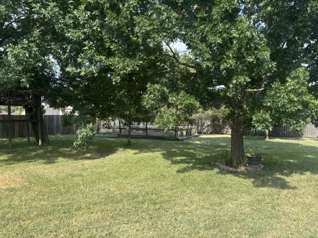 Expansive backyard with a manicured lawn, featuring mature trees providing ample shade