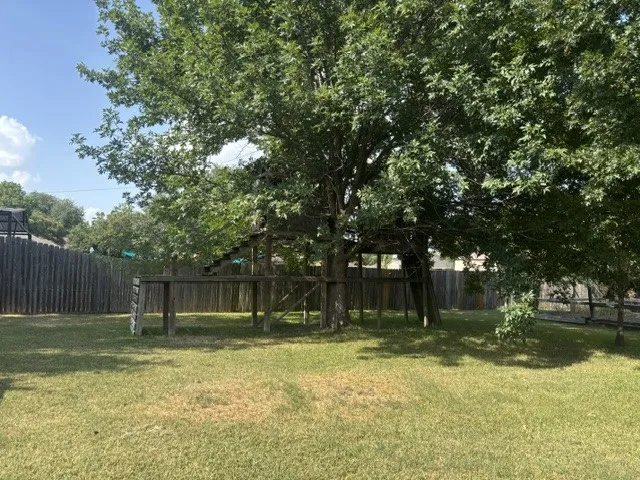 Spacious backyard featuring a substantial mature tree with a built-in wooden play structure