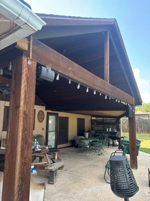 Expansive covered patio featuring a high vaulted ceiling, exposed wood beams, and a concrete slab foundation