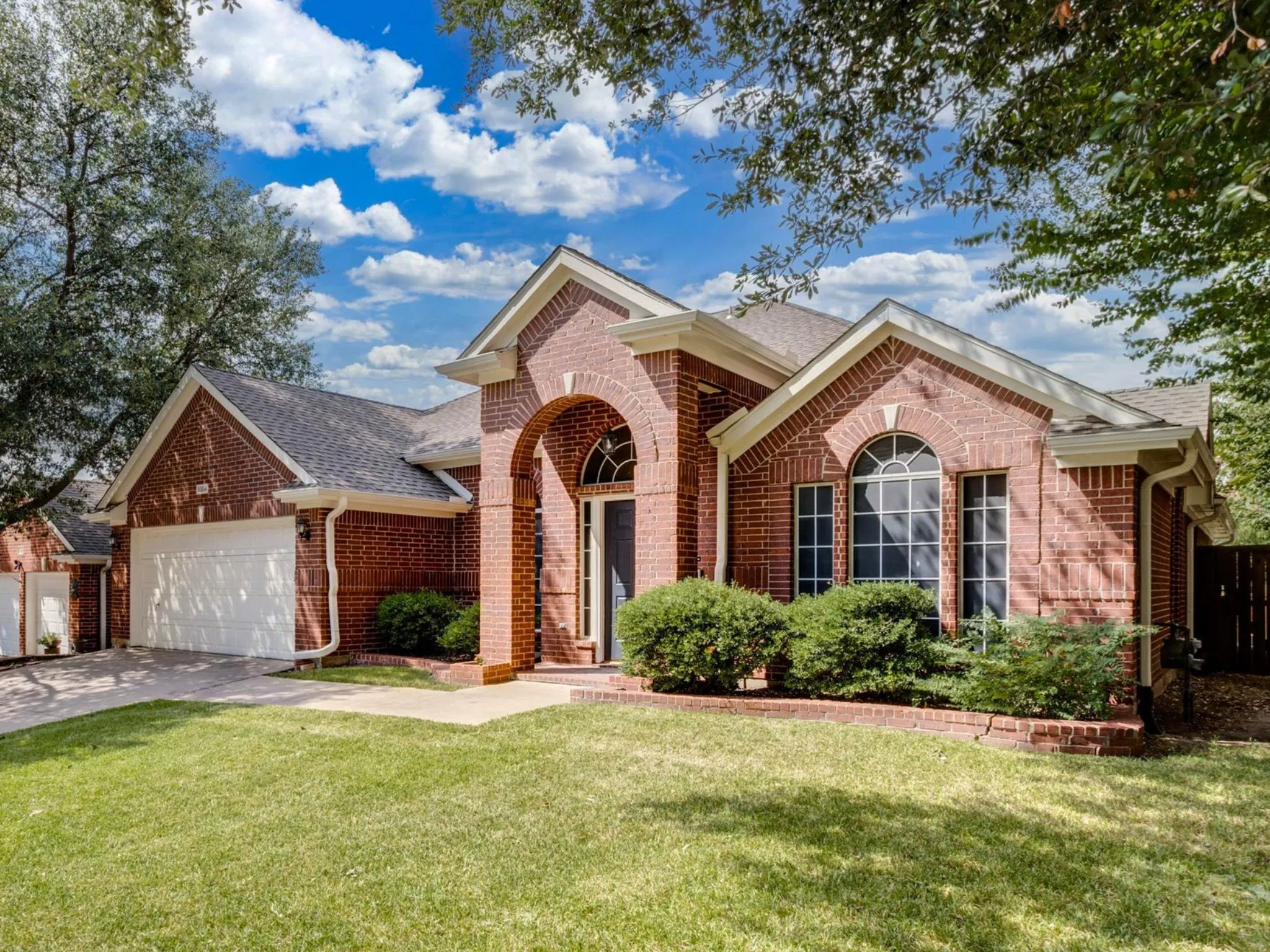Brick exterior featuring an arched entry, prominent arched window, and attached garage