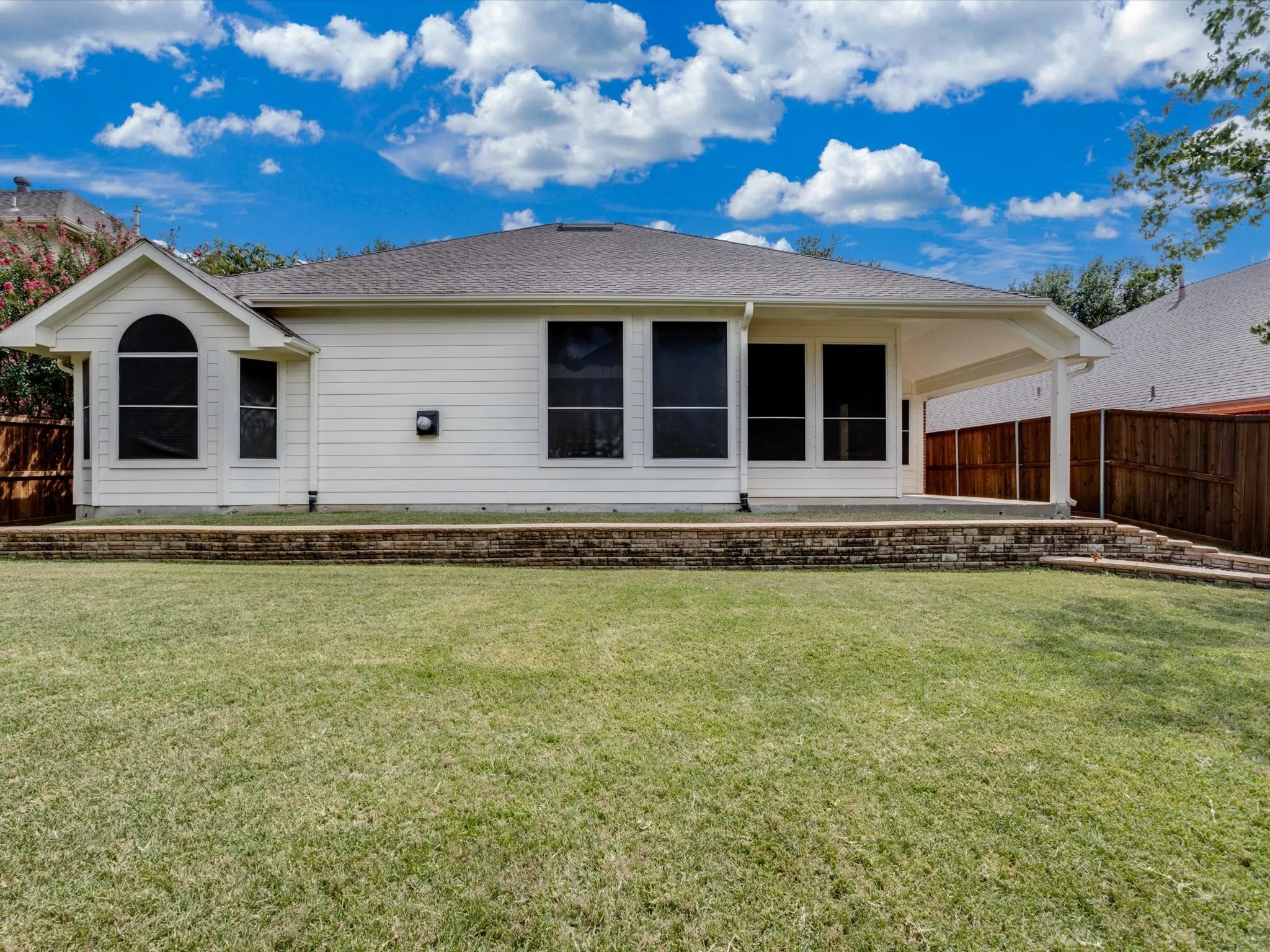Expansive backyard featuring a stone retaining wall, covered patio, and privacy fencing