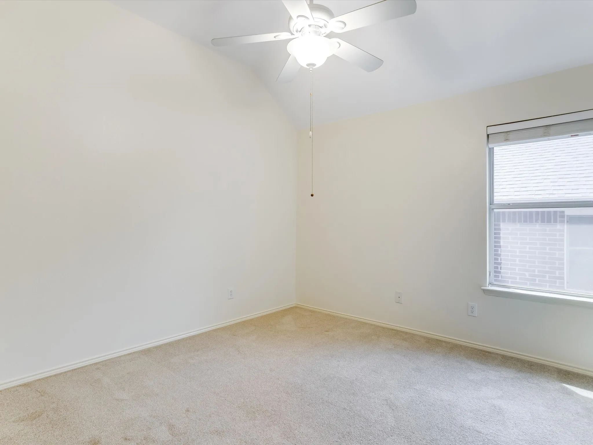 Bright bedroom featuring neutral carpeting, ceiling fan with integrated lighting, and large window with blinds allowing natural light throughout the space