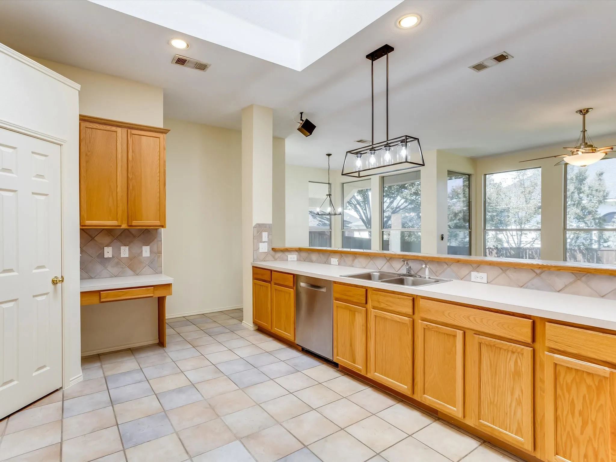 Kitchen featuring light wood cabinetry, a double basin stainless steel sink, and light-toned tile flooring