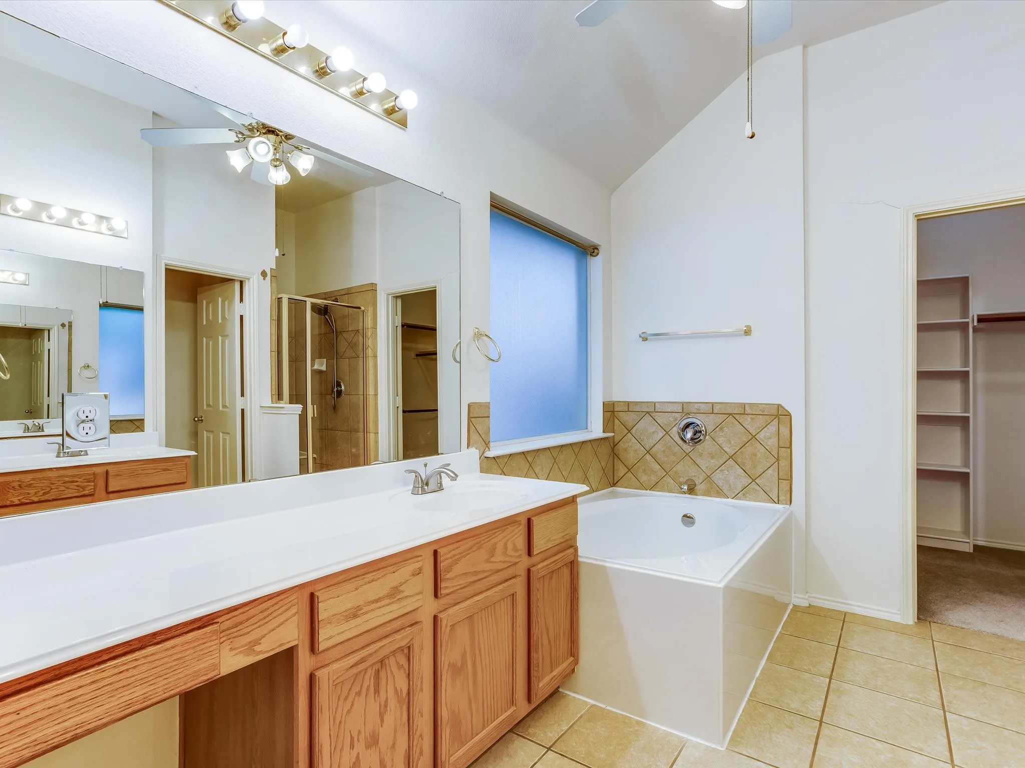 Bathroom featuring a built-in tub with tile surround, a dual vanity with light wood cabinetry, and a glass-enclosed shower