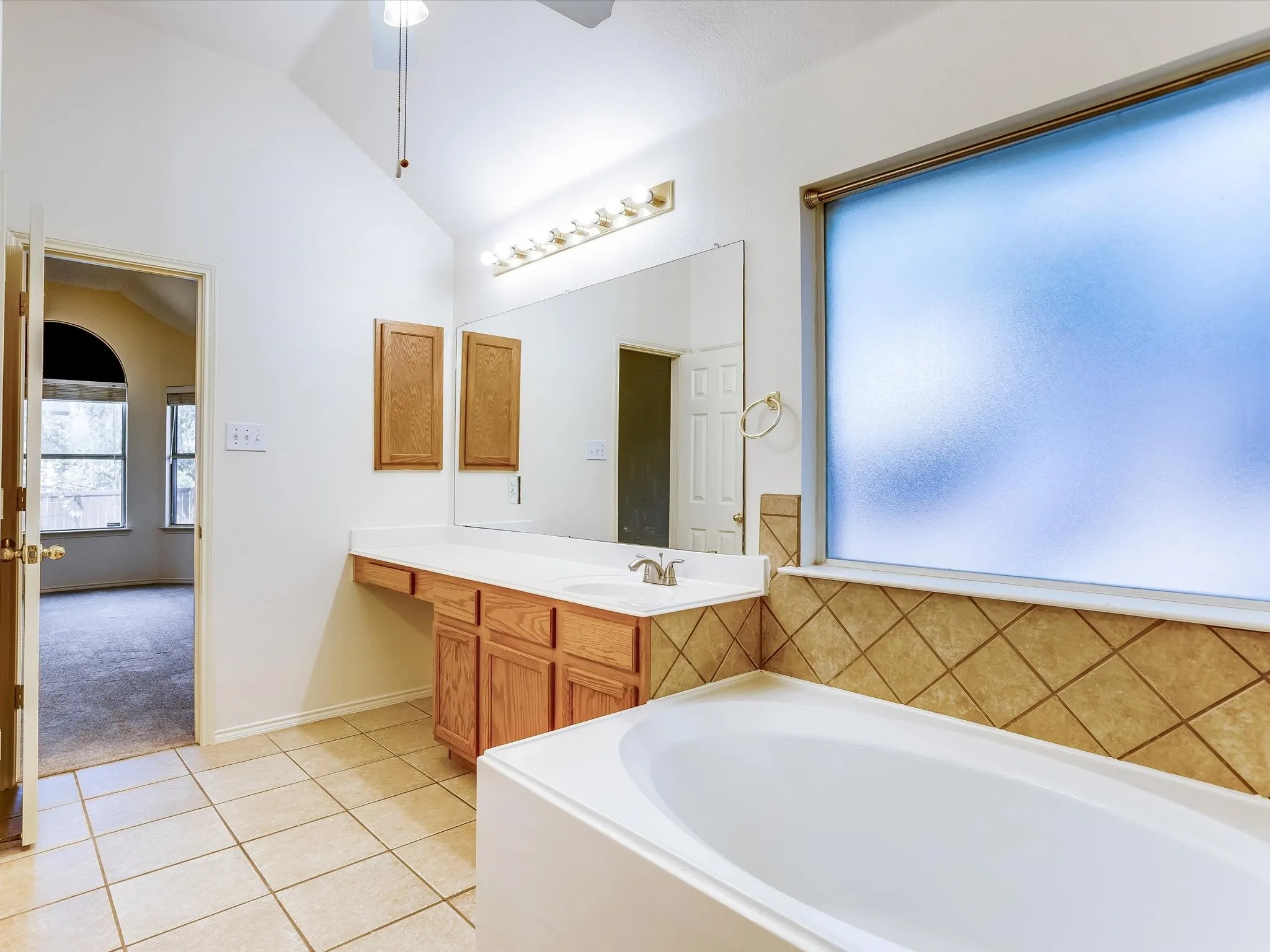 Bathroom featuring a full-size built-in bathtub, a window with obscure glass, and a vanity with a white countertop and natural wood cabinetry