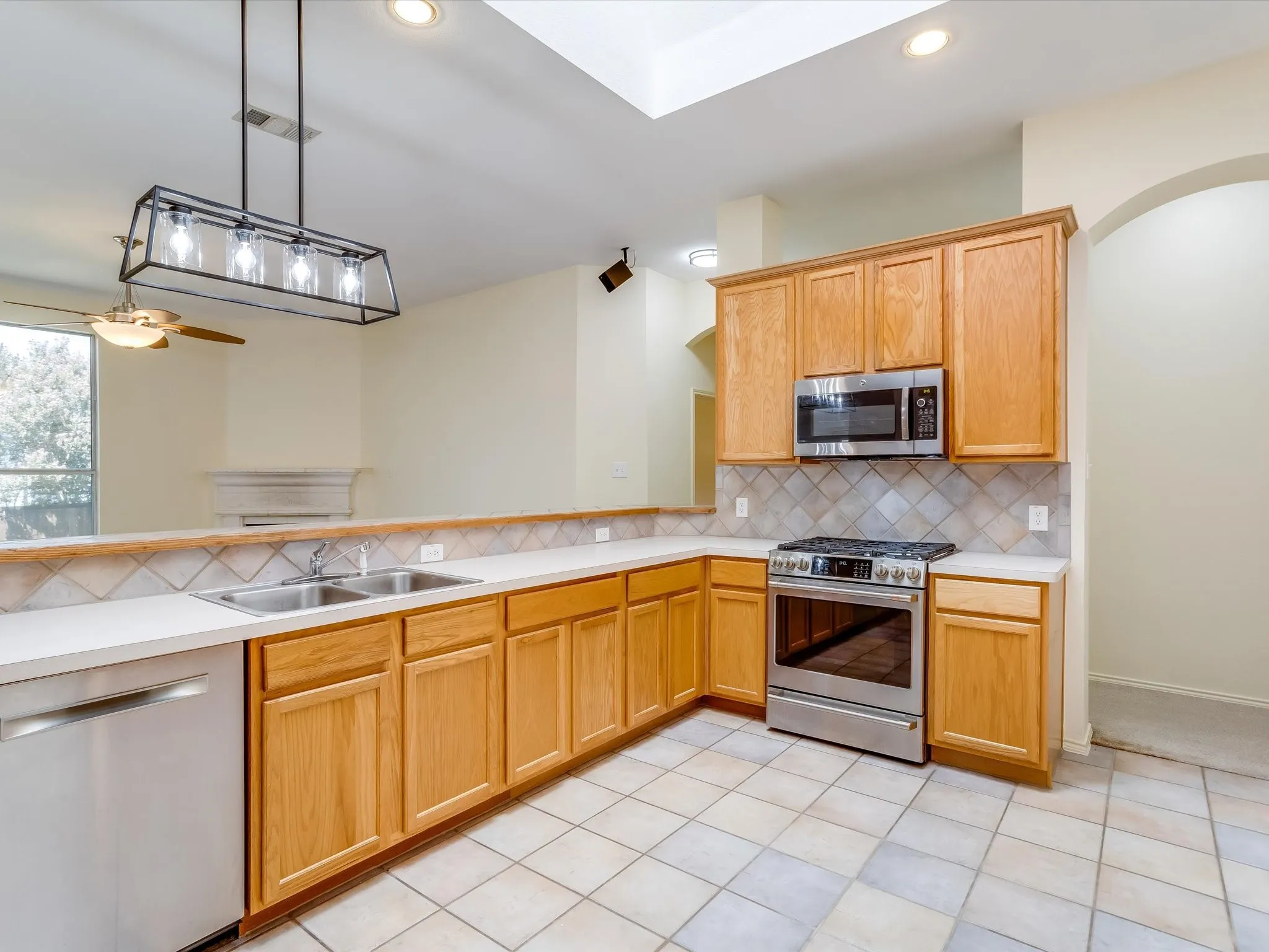 U-shaped kitchen featuring wood cabinetry, stainless steel appliances, a double basin sink, light-toned countertops, and a tiled backsplash